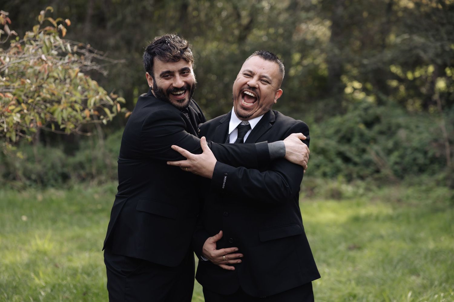 Joyful groomsmen embracing and celebrating in an outdoor wedding setting.