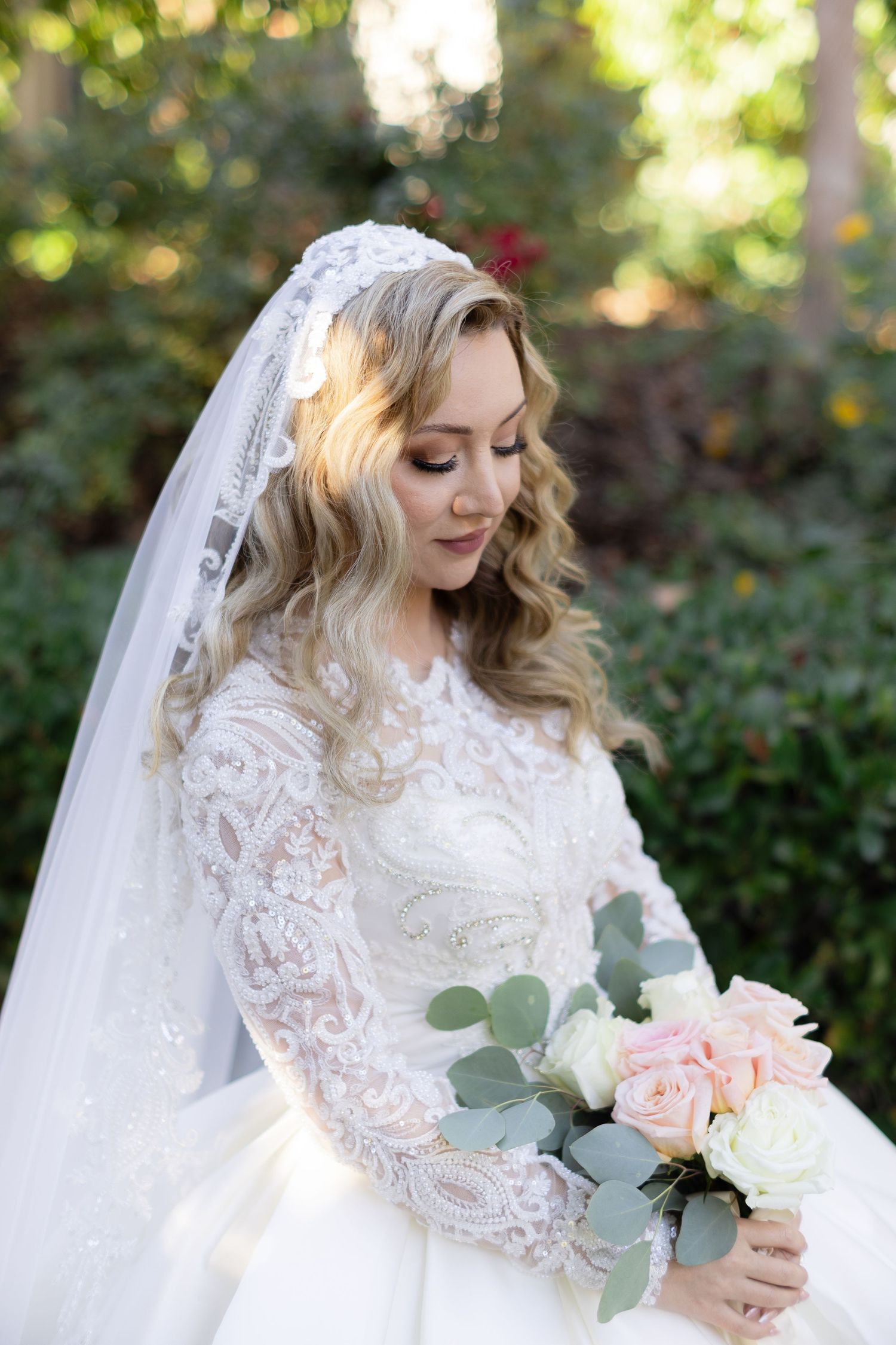 A bride in a long-sleeved lace wedding gown holds a pink and white rose bouquet with eucalyptus accents.
