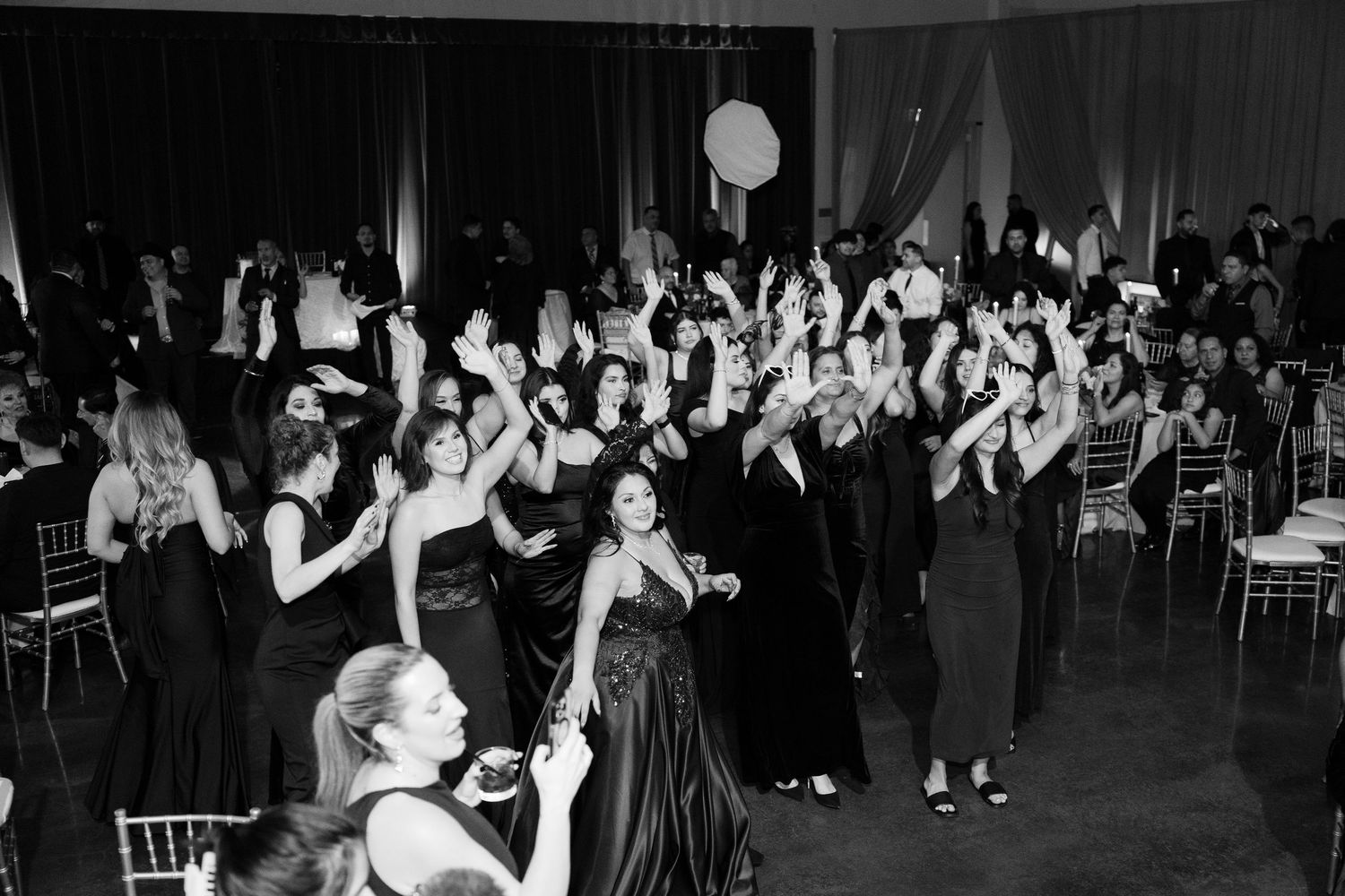 A black and white photo shows wedding guests with raised arms celebrating on the dance floor.