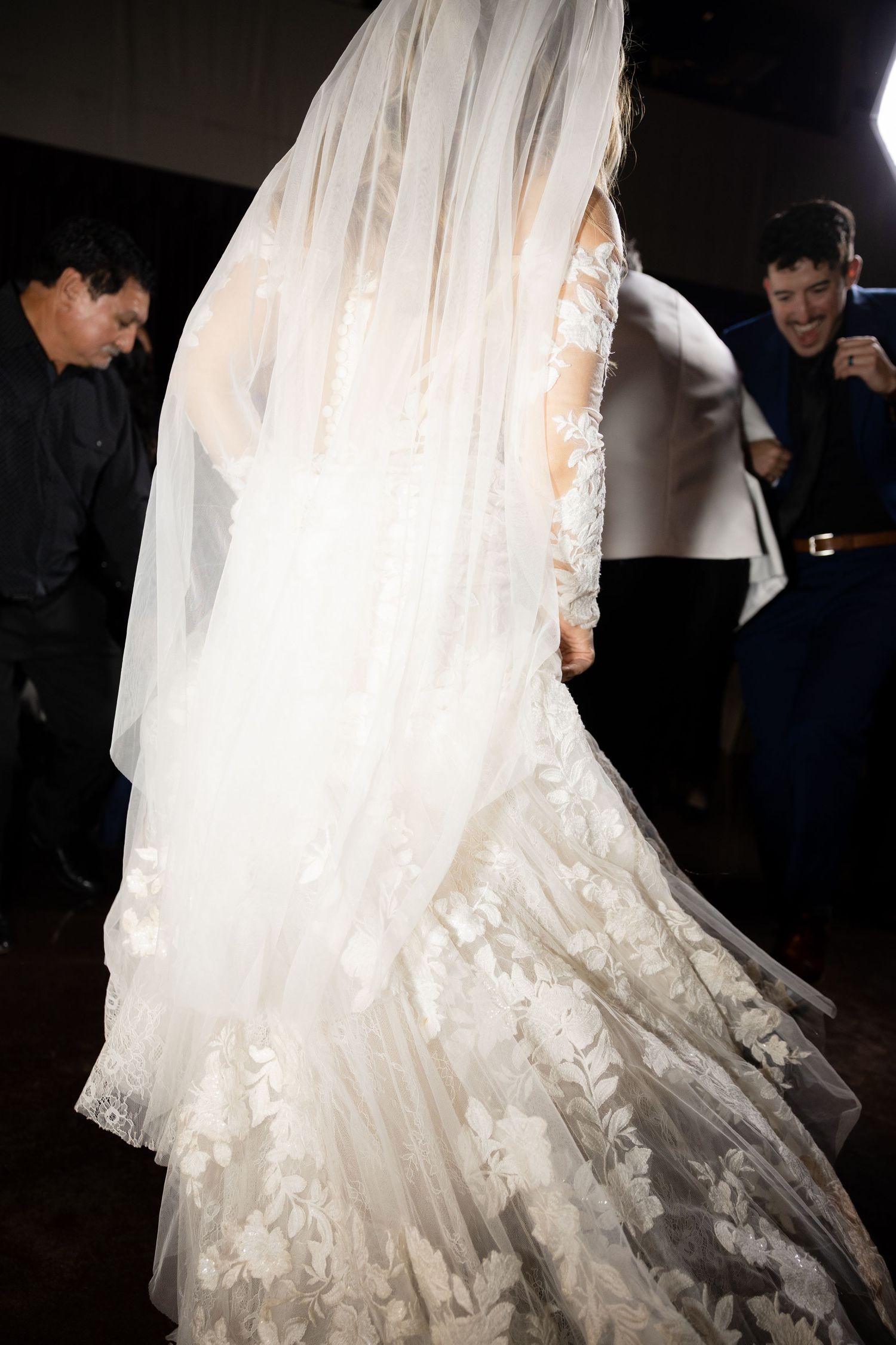 Elegant white wedding dress with lace details and flowing veil captured in dramatic lighting.