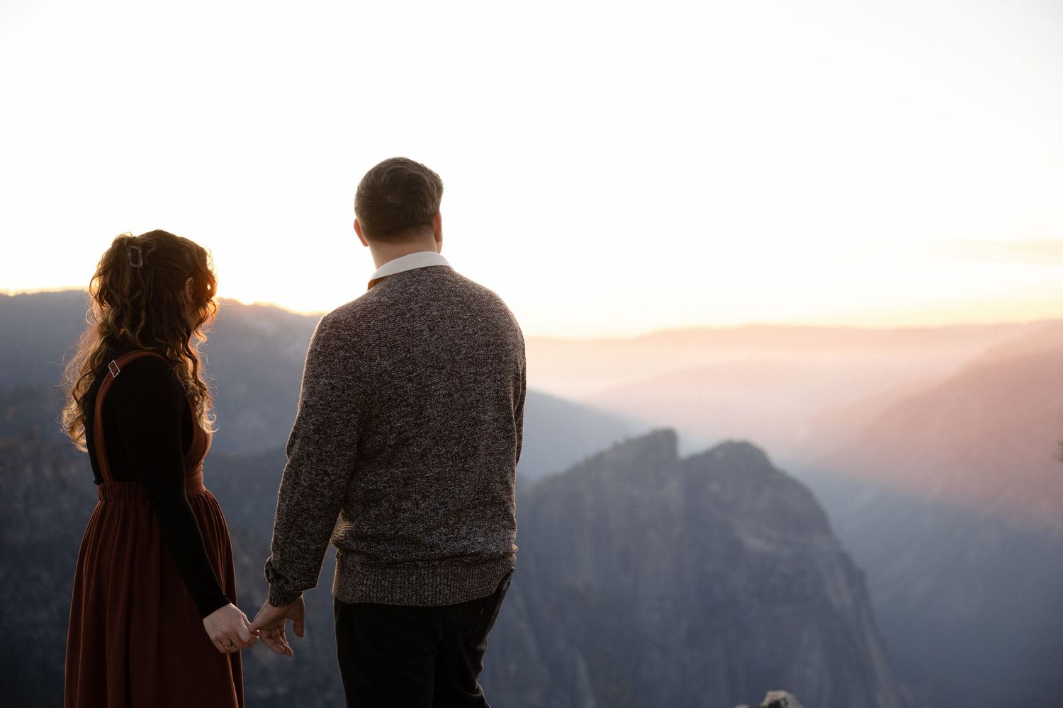 A couple stands close together on a mountain vista point during sunset.