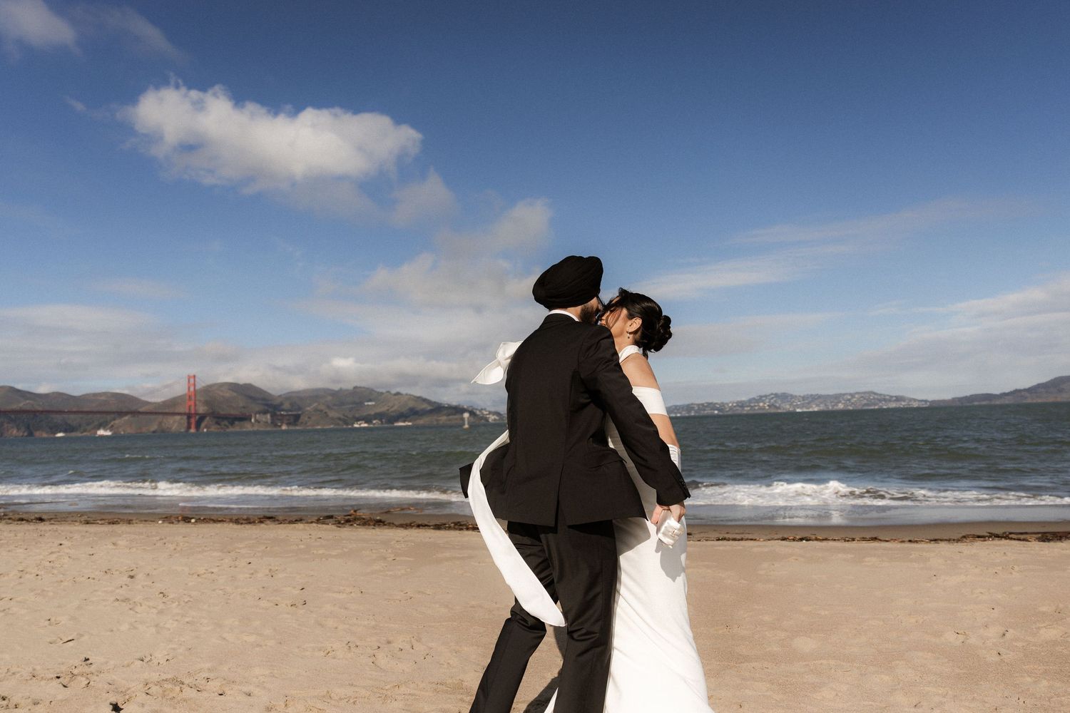 A couple shares romantic moments on a scenic beach with mountains and ocean views in the background.