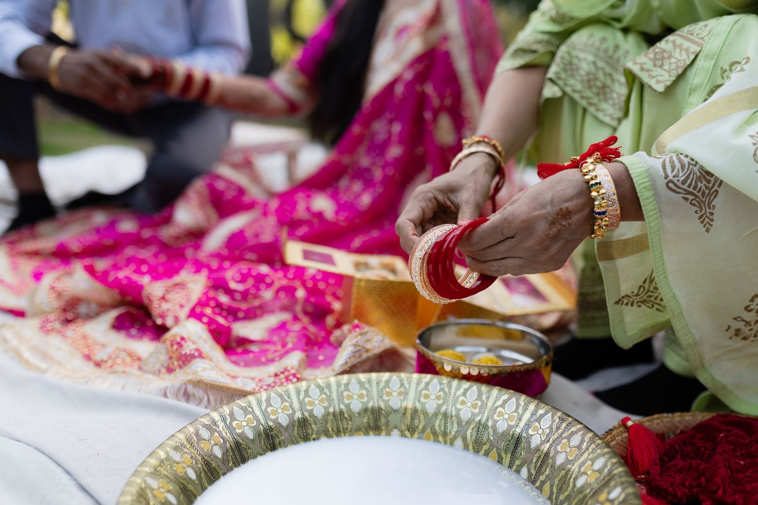 Hands prepare traditional Indian food and spices during a cultural ceremony with bright pink decorative elements.
