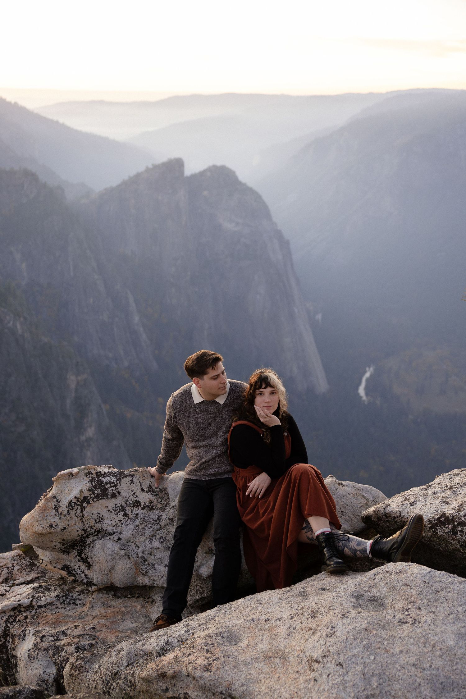 Two people share a tender moment while resting on a rocky mountain overlook.
