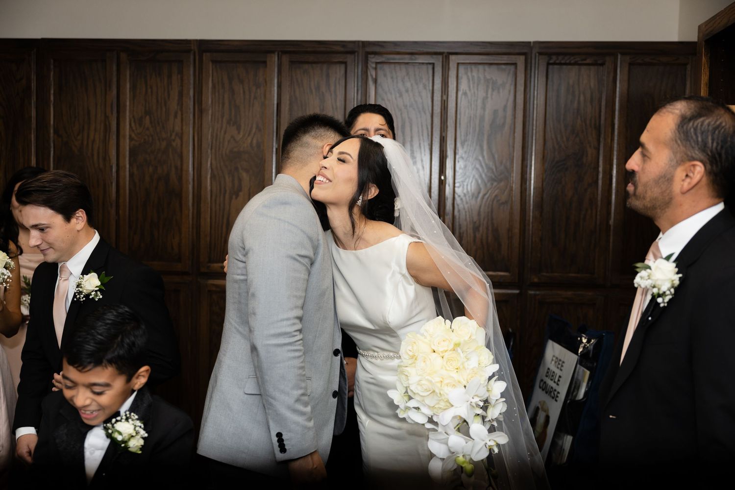 Wedding party members gathered in an elegant wood-paneled room with formal attire.