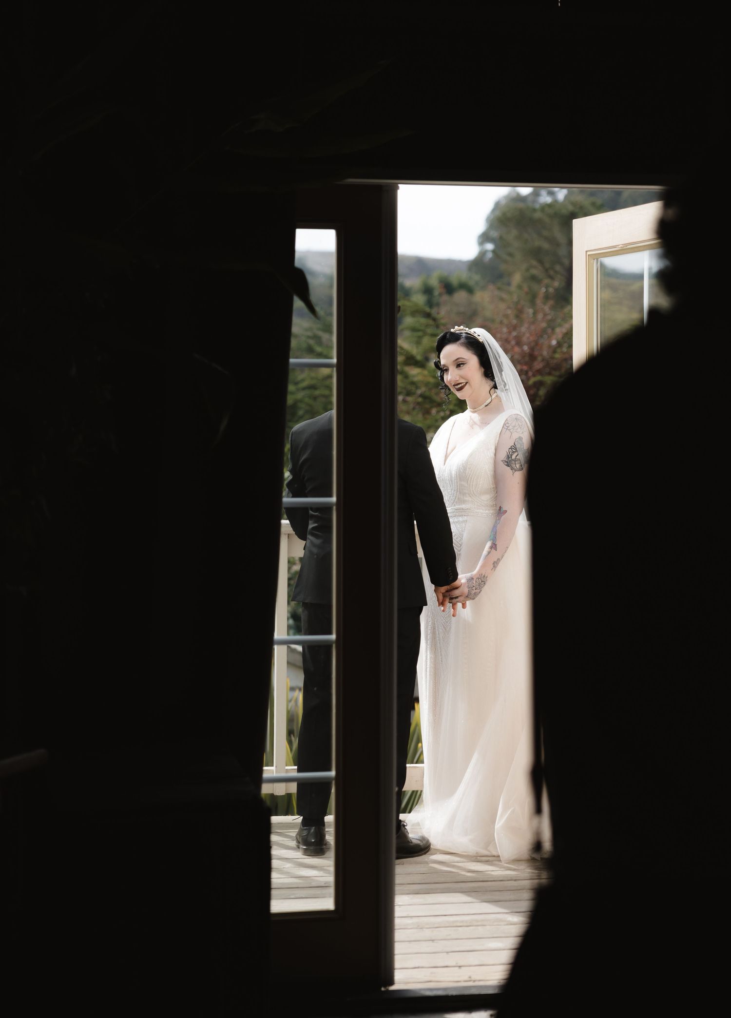 Candid wedding photo through doorway showing bride in full-length gown on porch.