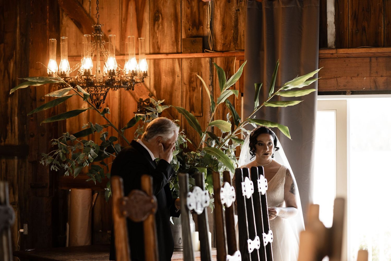 Rustic barn wedding venue interior with hanging lights and greenery decorations.