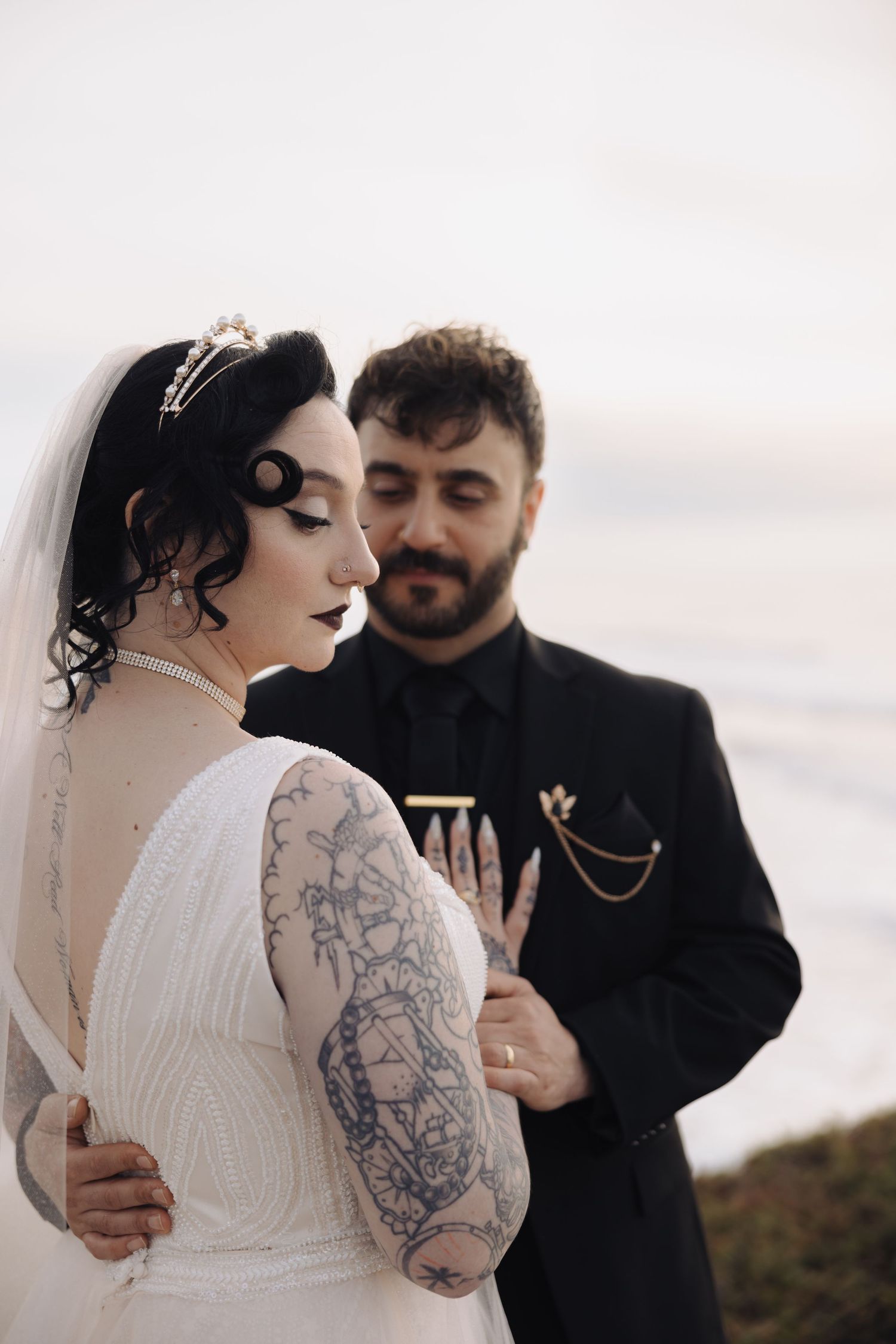 Intimate wedding moment captured on a beach with flowing white dress and black attire.