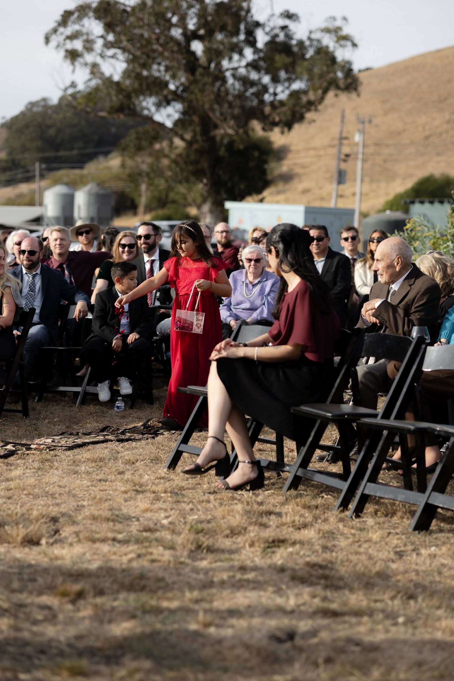 Wedding guests seated in rows of chairs on a grassy hillside during an outdoor ceremony.