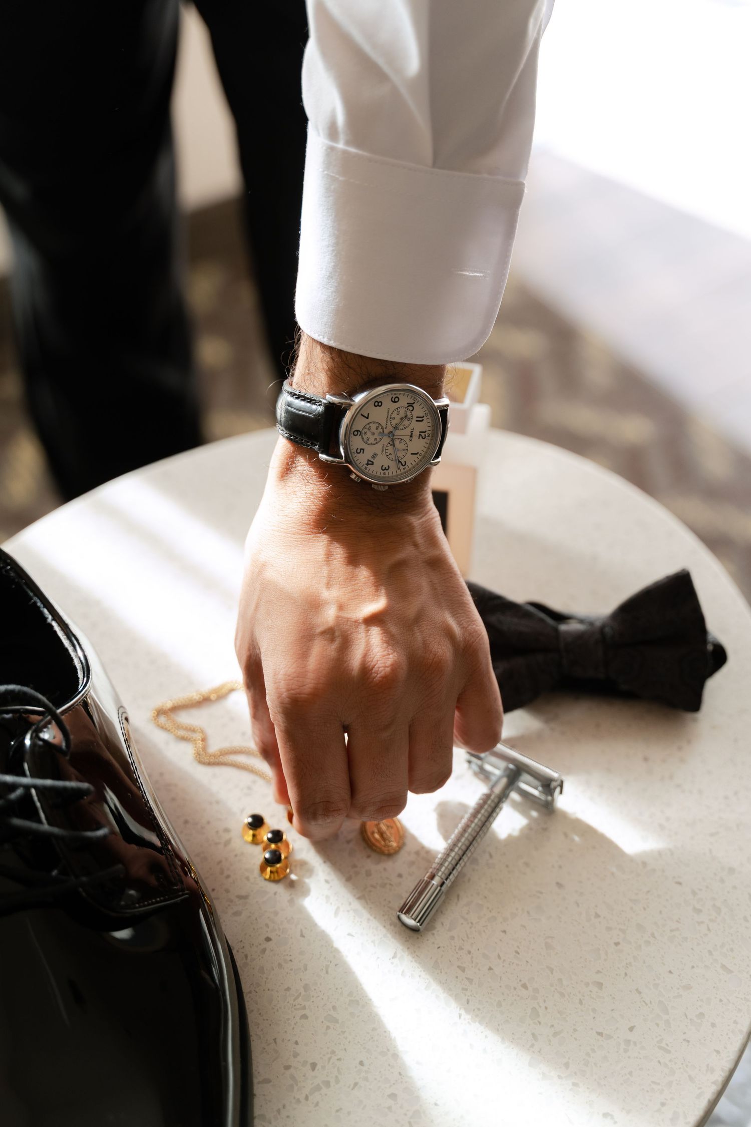 Hands arranging accessories and jewelry on a white surface in natural light.