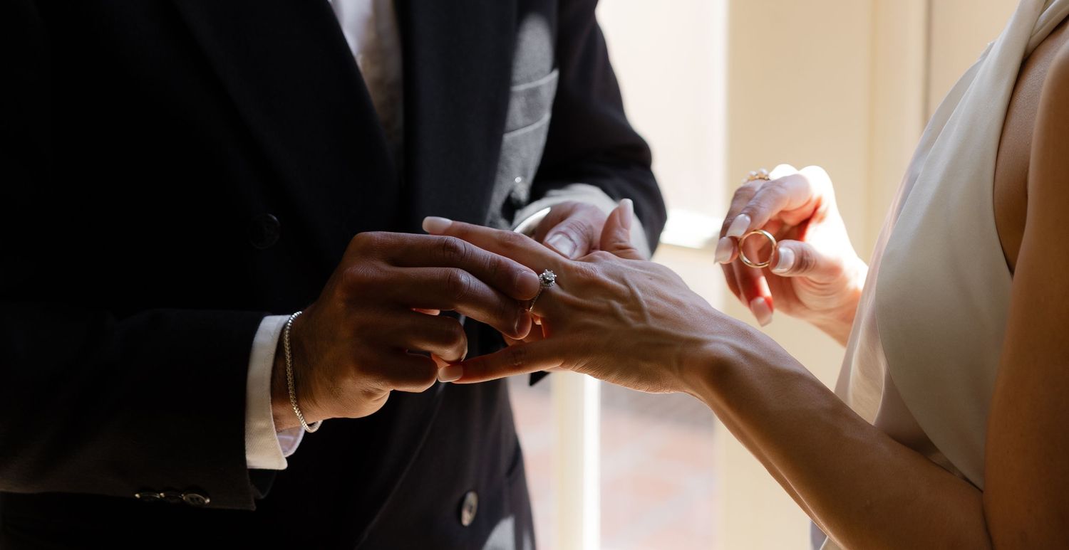 Couple exchanging wedding rings during a romantic ceremony, close-up of hands placing gold band on finger.