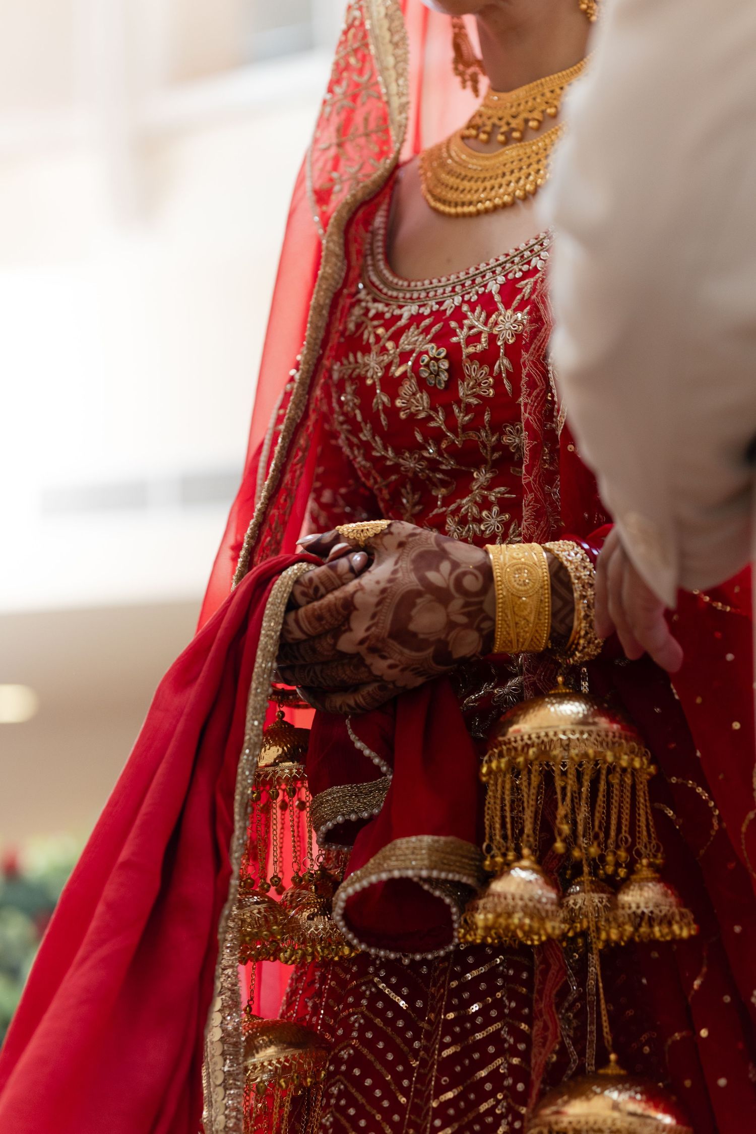 Close-up detail of traditional Indian bridal attire showing red embroidered fabric, gold jewelry and decorative tassels.
