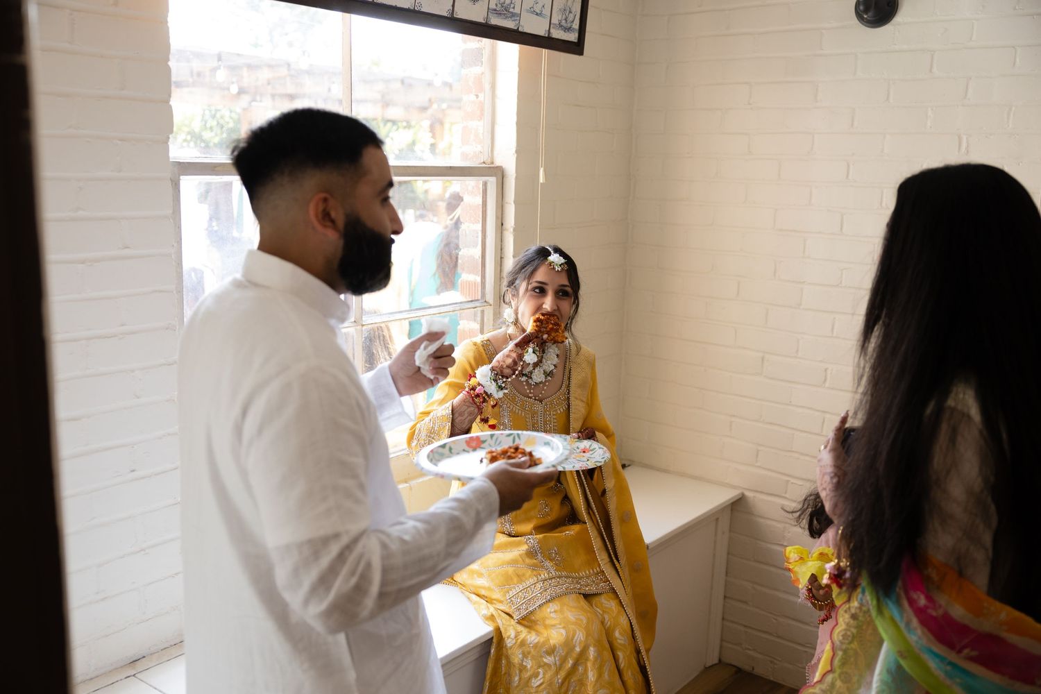 People gather in a bright room for a meal, with traditional Indian attire and food being served at the table.