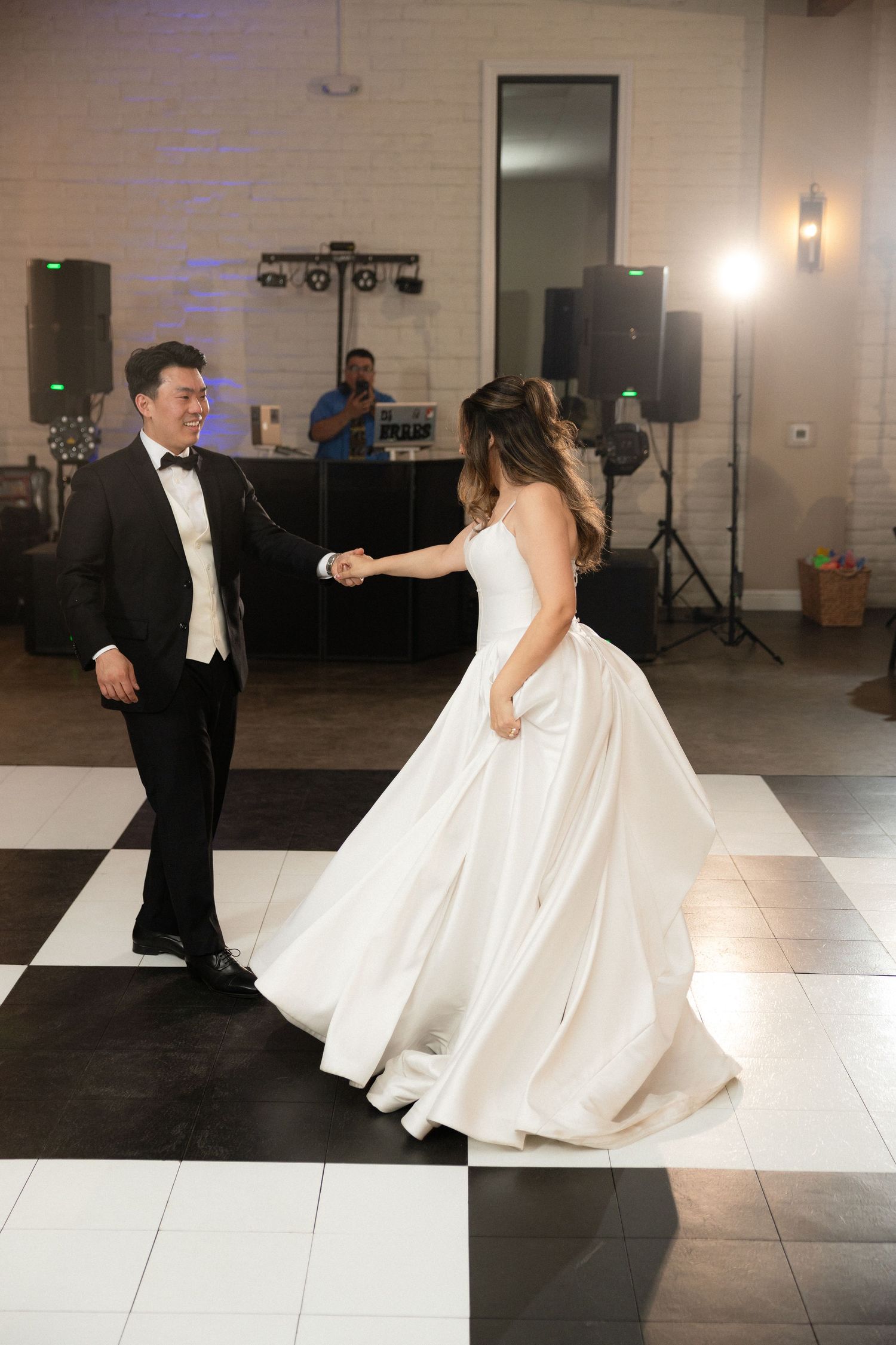 Bride and groom share their first dance on a black and white checkered dance floor at elegant wedding reception.