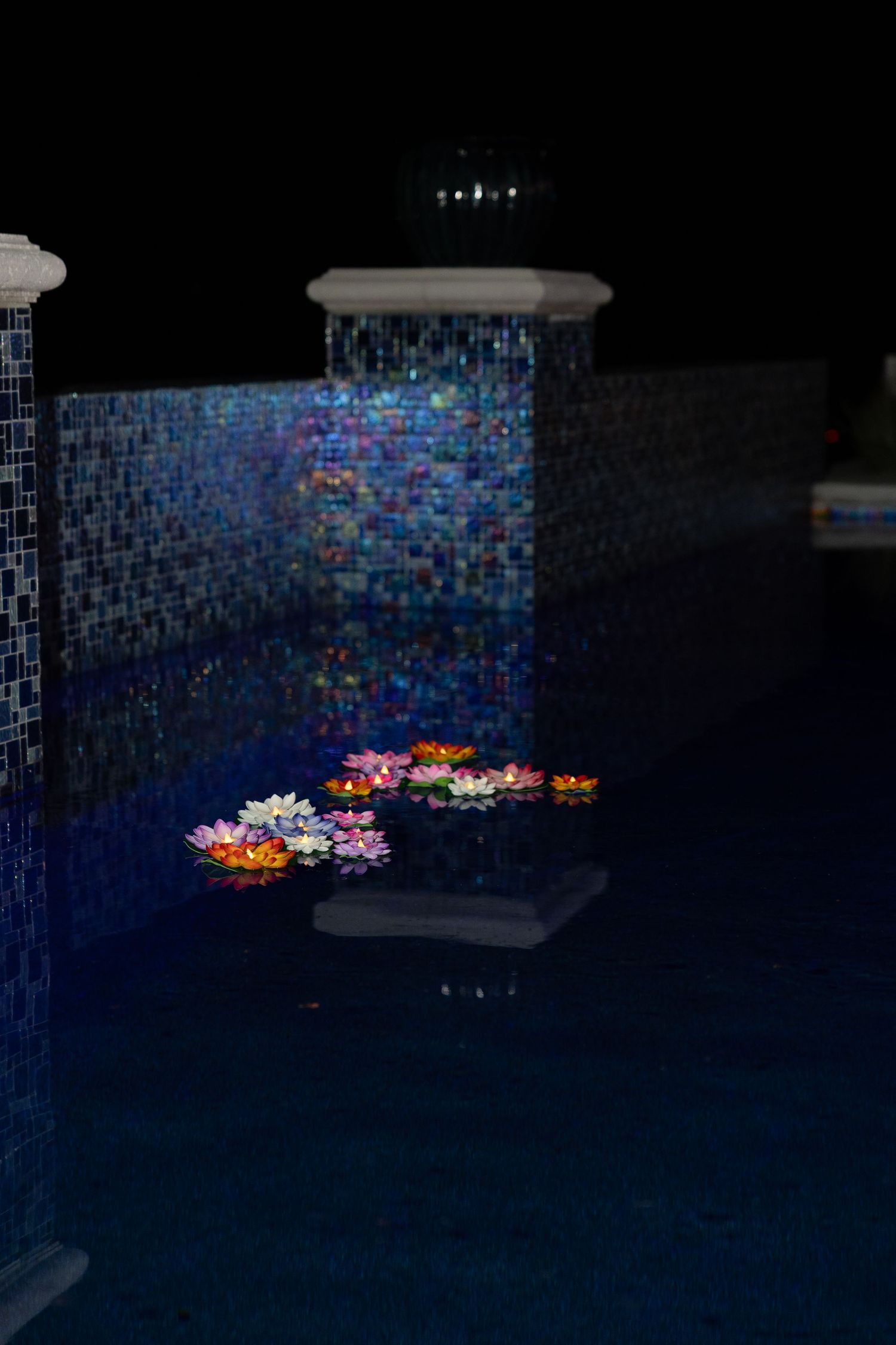 A series of illuminated lotus flowers floating in a dark pool against a blue mosaic tile background.