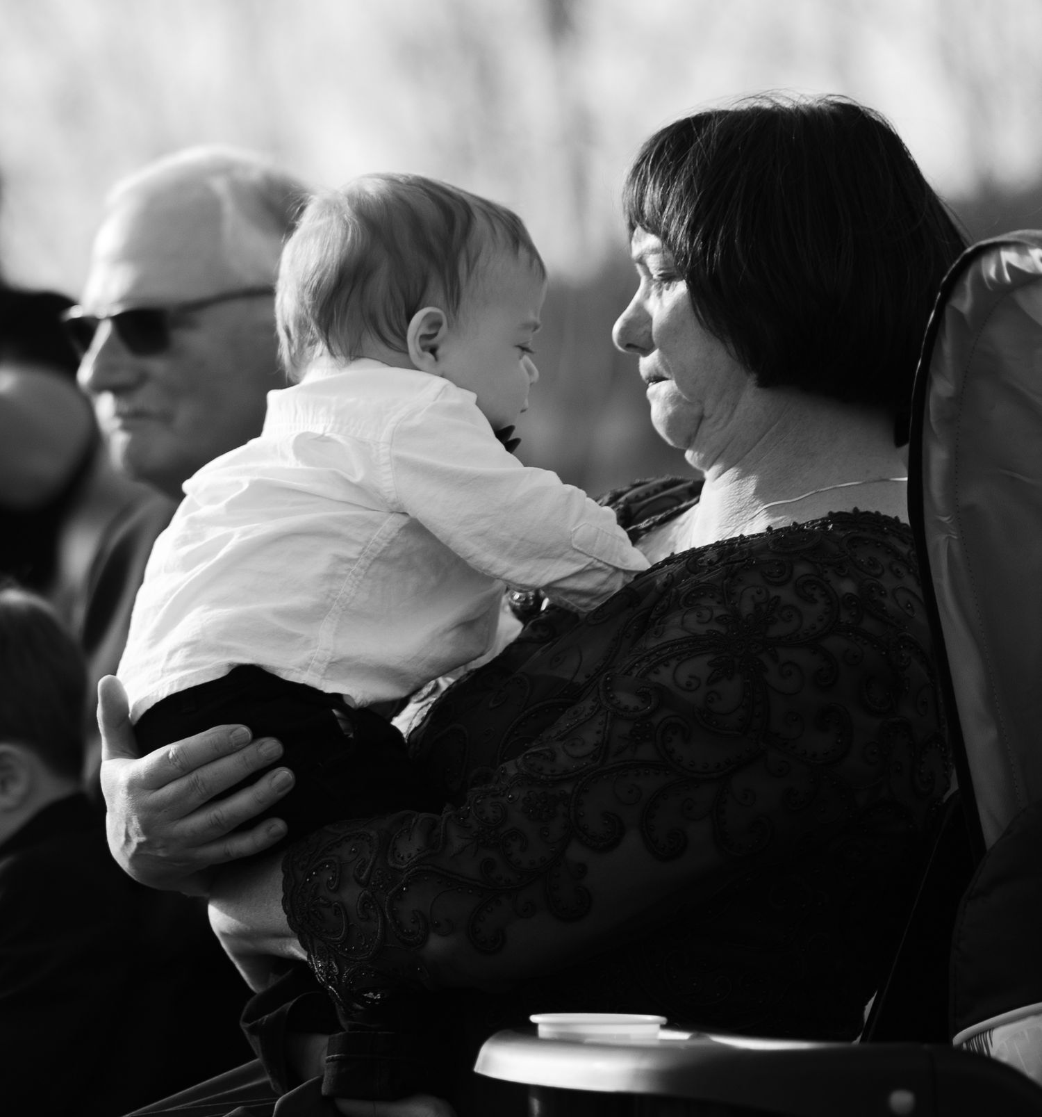 A tender moment between a baby in white and a guest during an outdoor wedding ceremony.