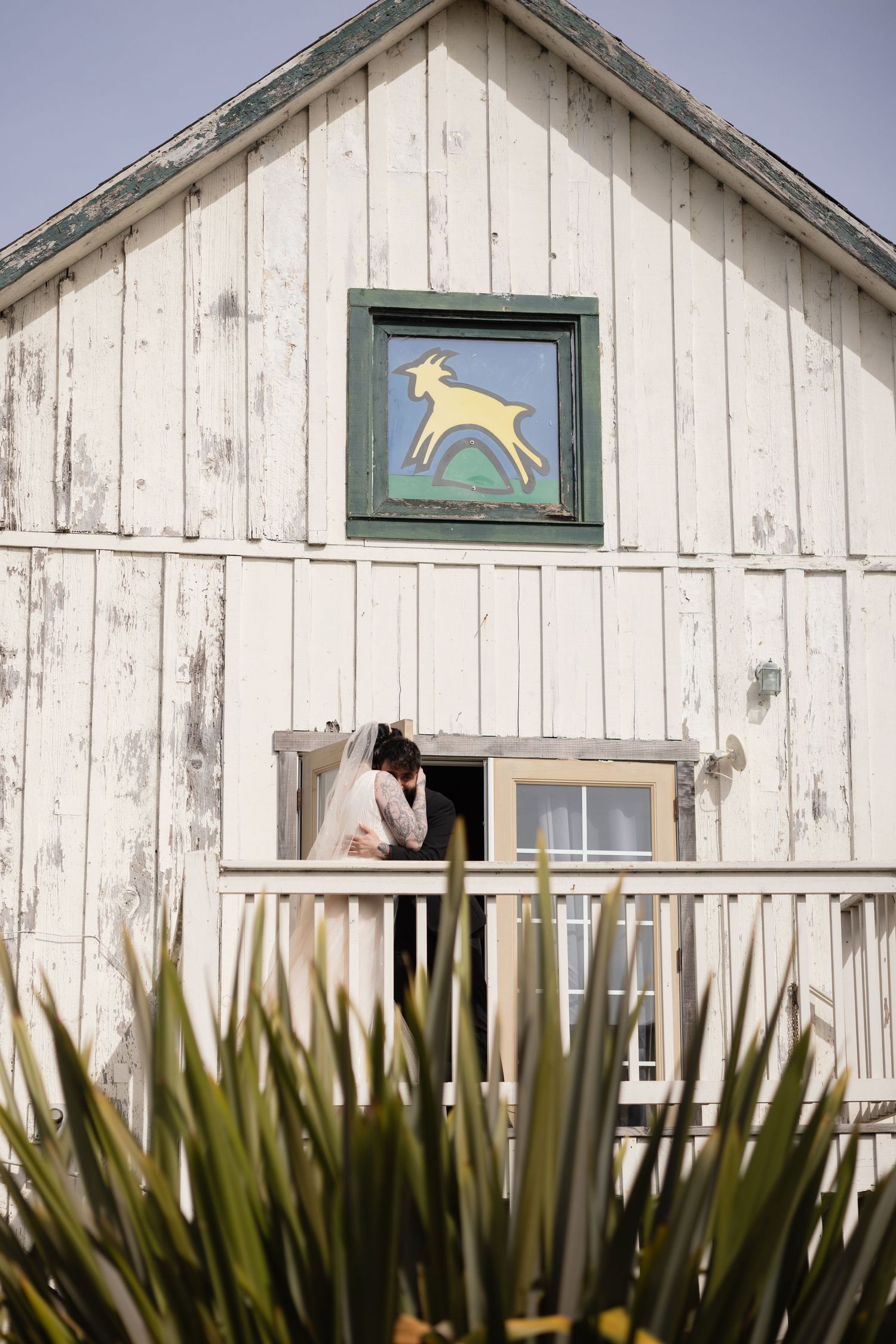 Two people stand close together on a farmhouse deck beneath a folk art deer sign.