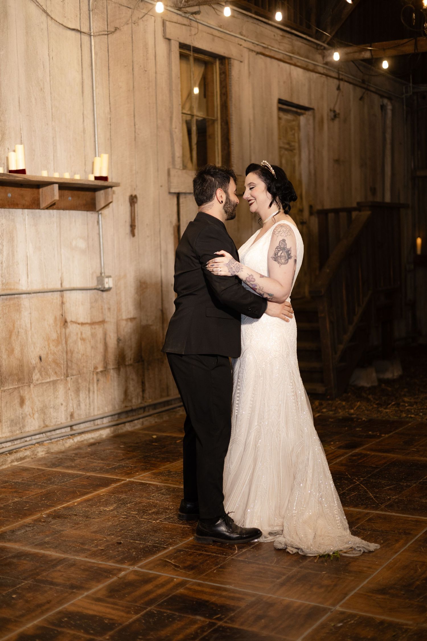 A couple shares an intimate dance moment in a rustic barn venue with string lights overhead.