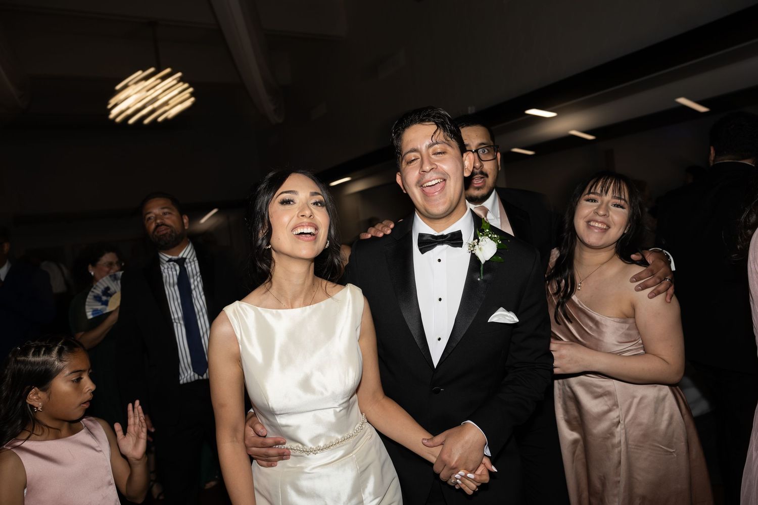 Wedding couple and guests celebrate joyfully on the dance floor at an indoor reception.