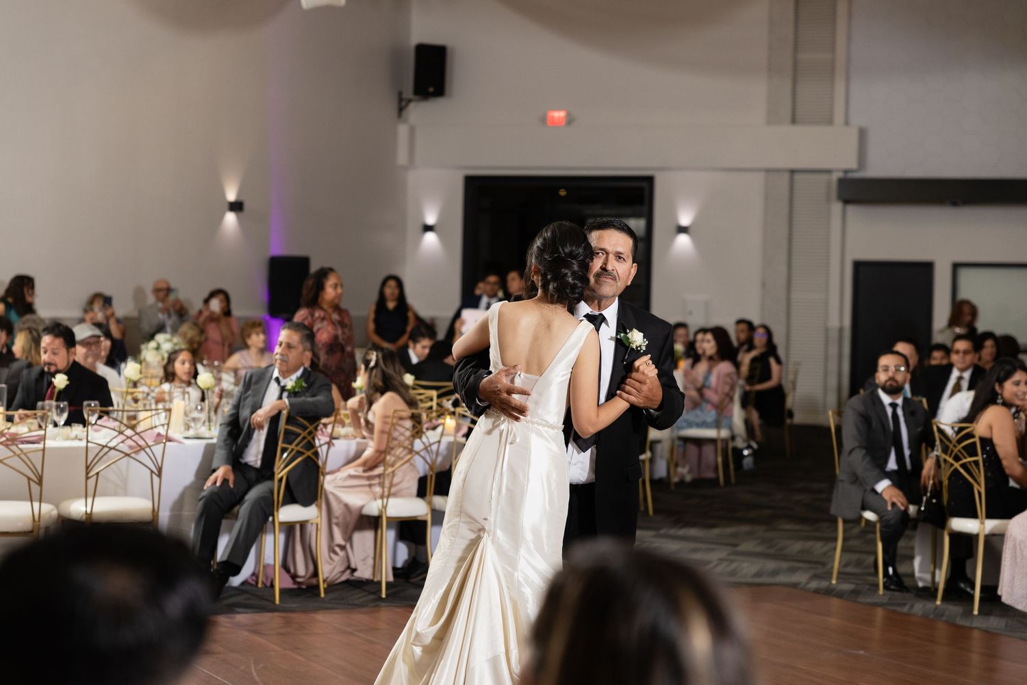 Spacious wedding reception hall with white draping and guests seated at round tables.