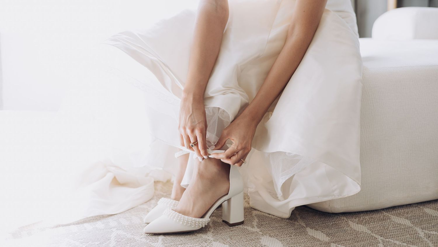 Detail shot of white bridal shoes and dress hem against light background.