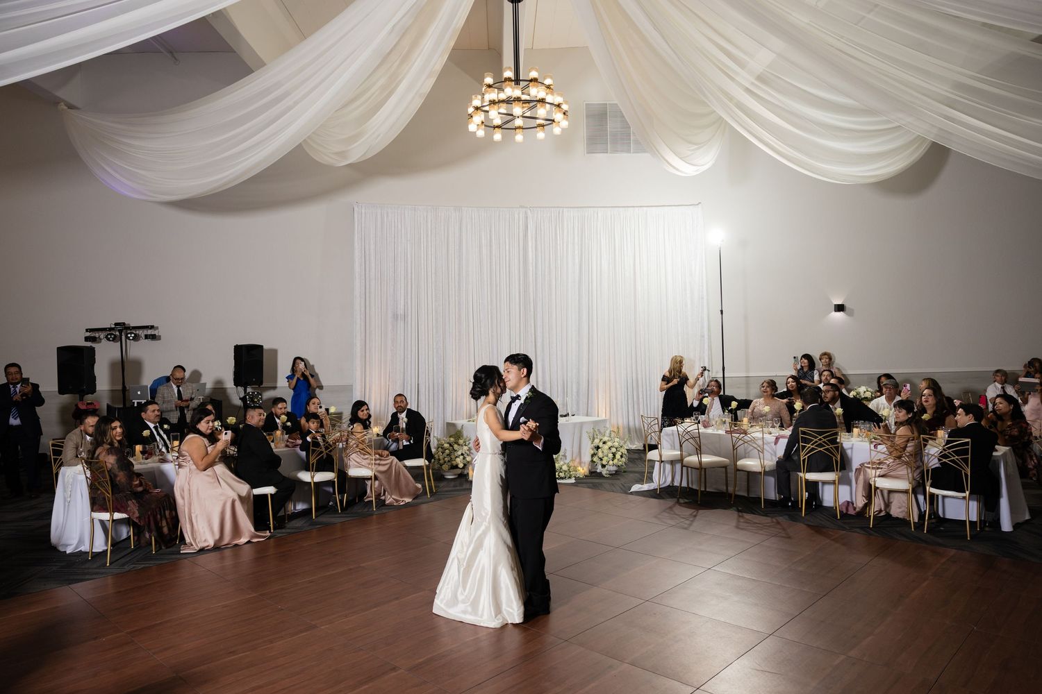 Wedding reception venue features stunning white ceiling draping and modern lighting fixtures.