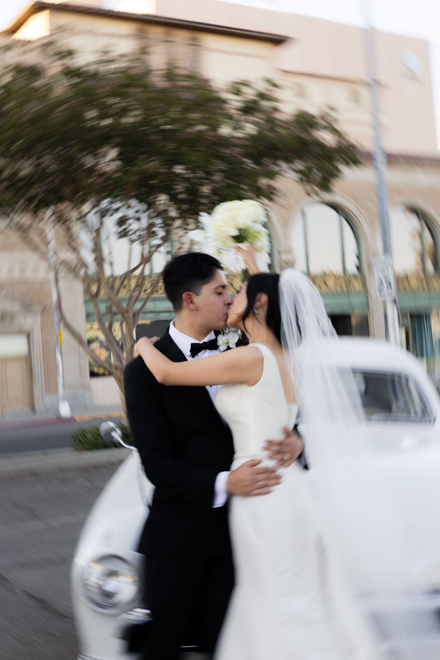 Newlyweds share a romantic dance in an outdoor setting with a flowing white wedding dress and classic tuxedo.