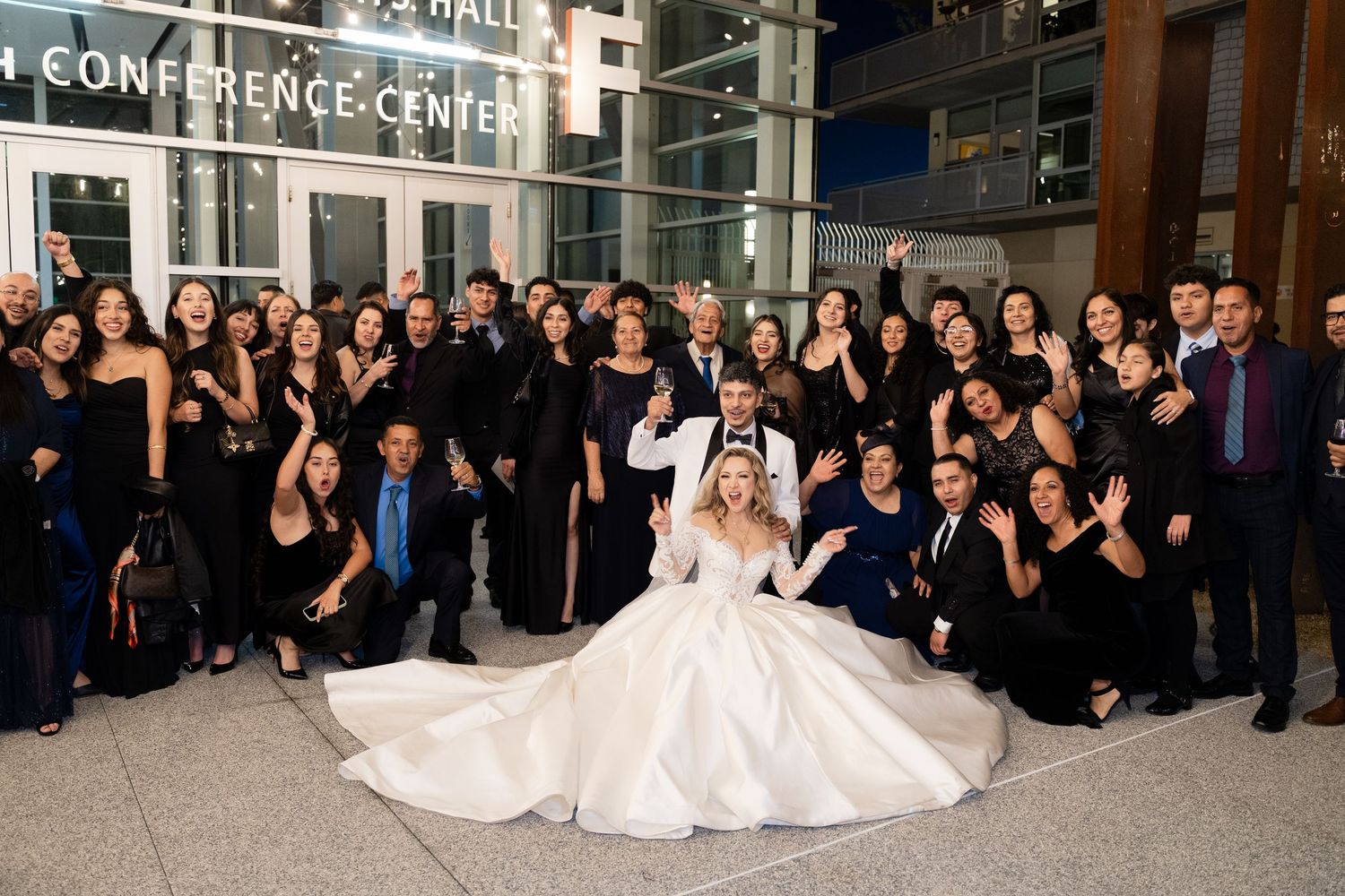 Wedding guests dressed in black pose for a group photo with the bride in white.