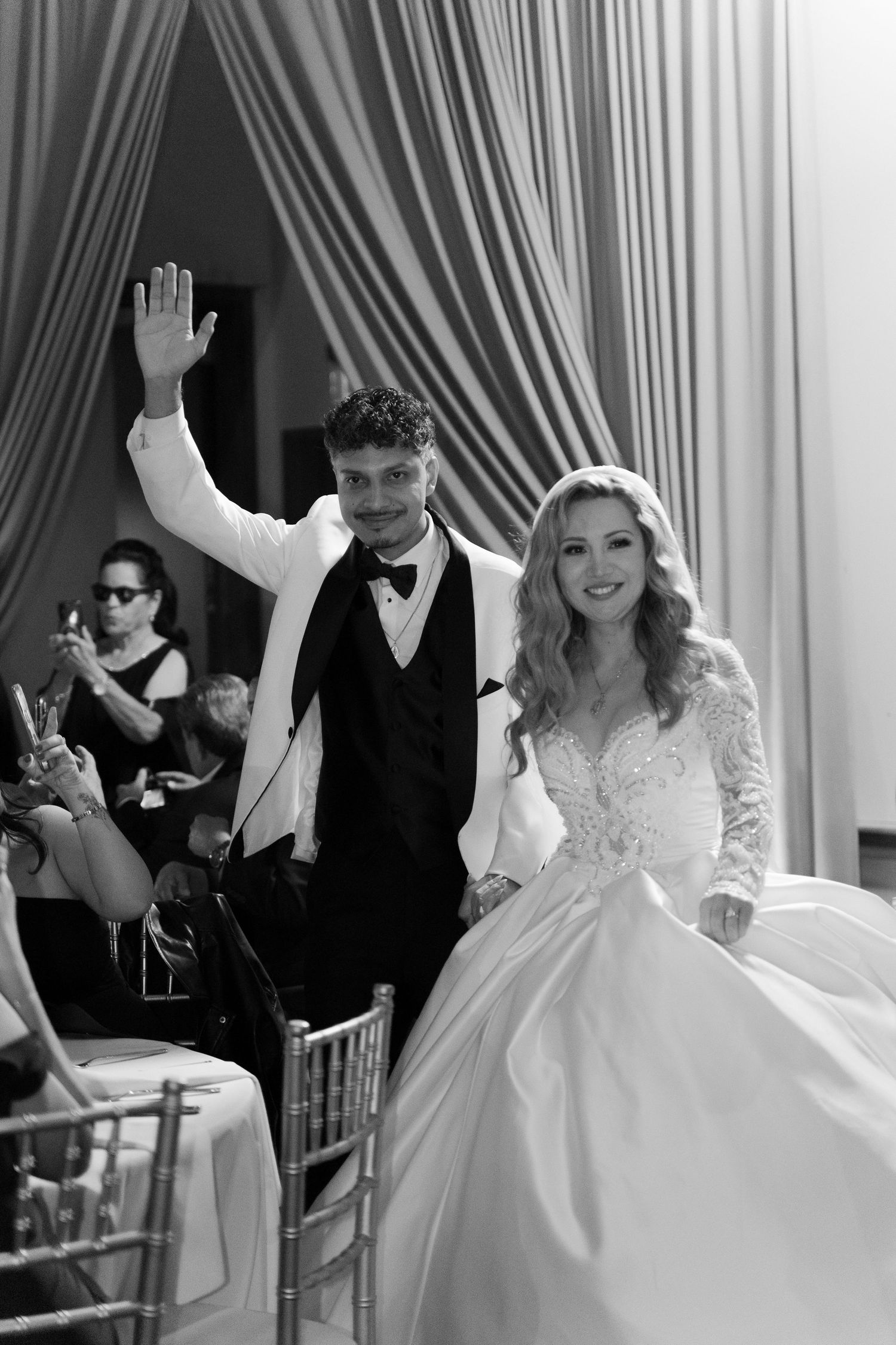 Wedding celebration with guests dancing and waving in a white-draped venue.