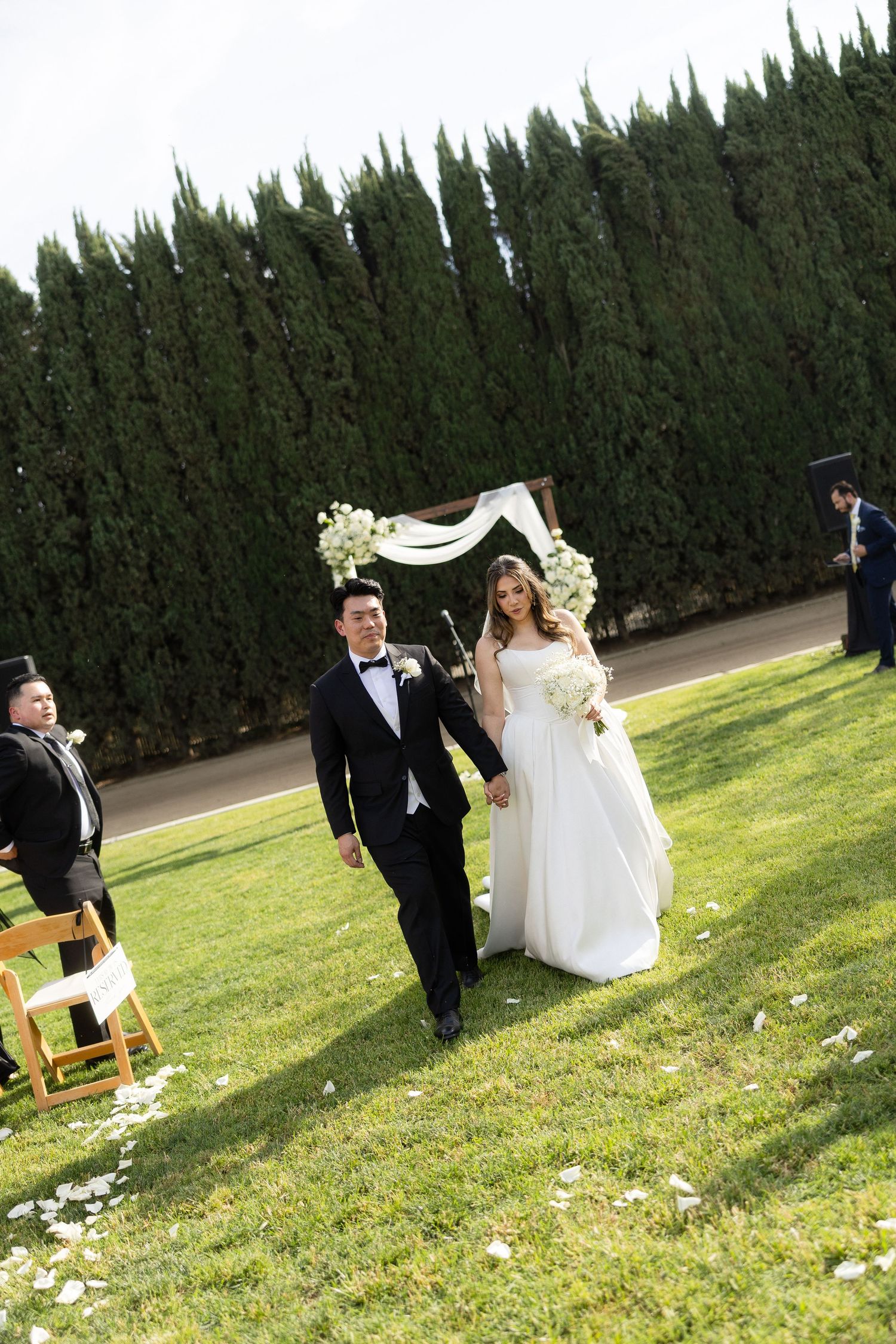 Newlywed couple walks down aisle hand in hand after outdoor garden wedding ceremony.