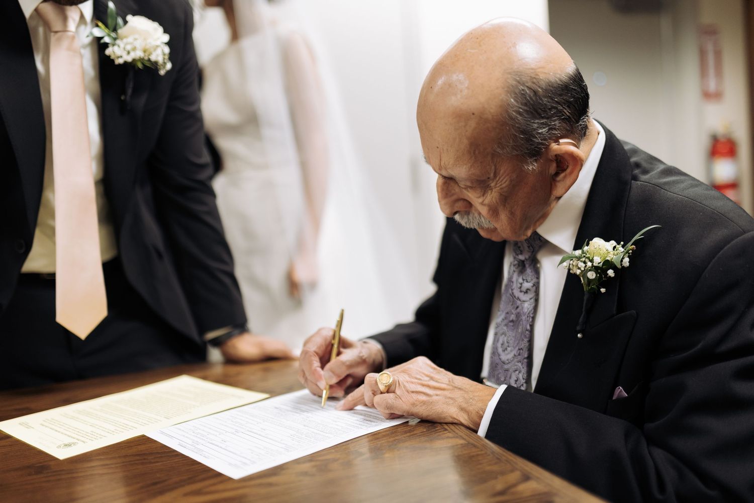 Close-up shots of hands signing wedding documents on a white tablecloth.