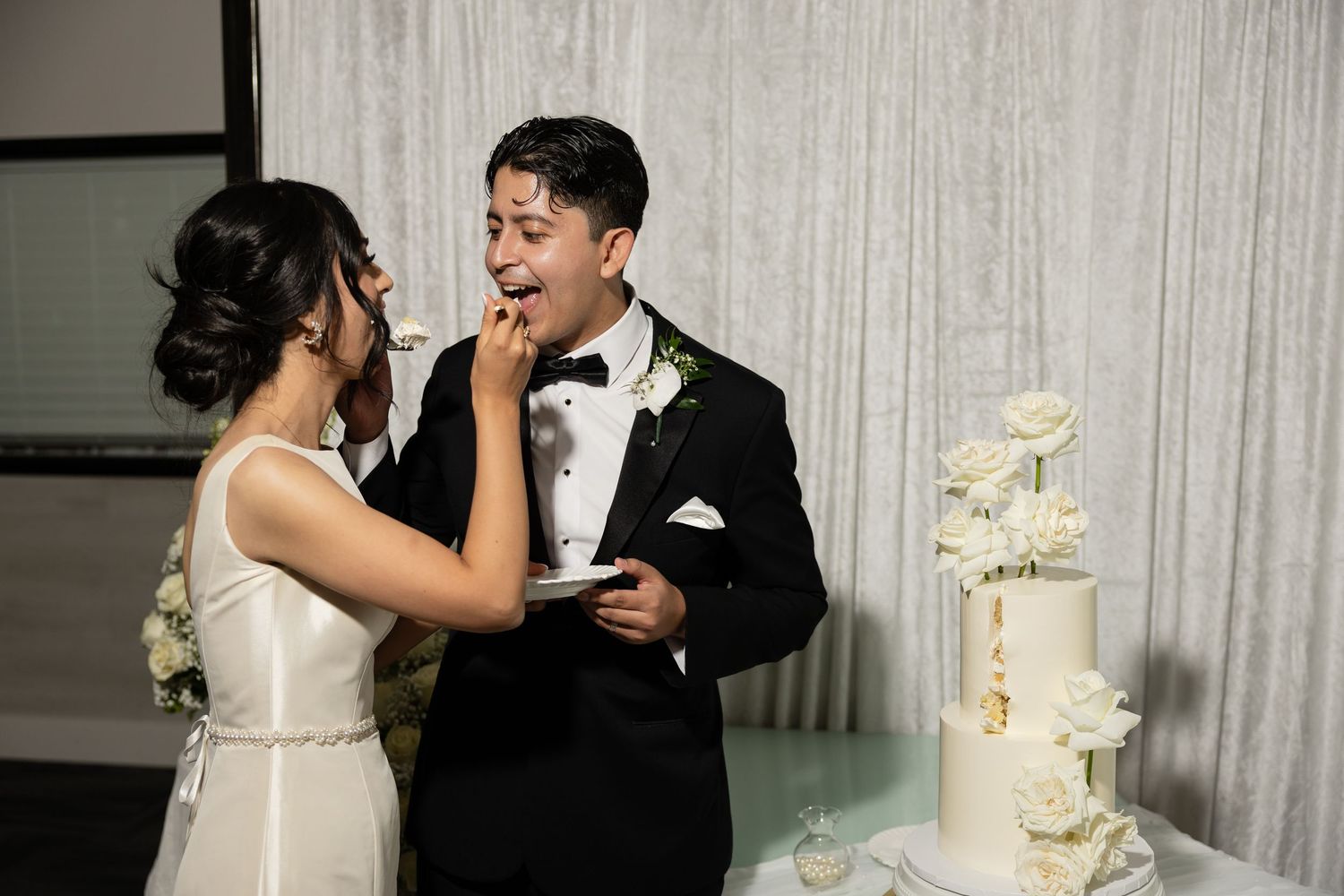 A couple shares a playful moment while cutting their wedding cake at their reception.
