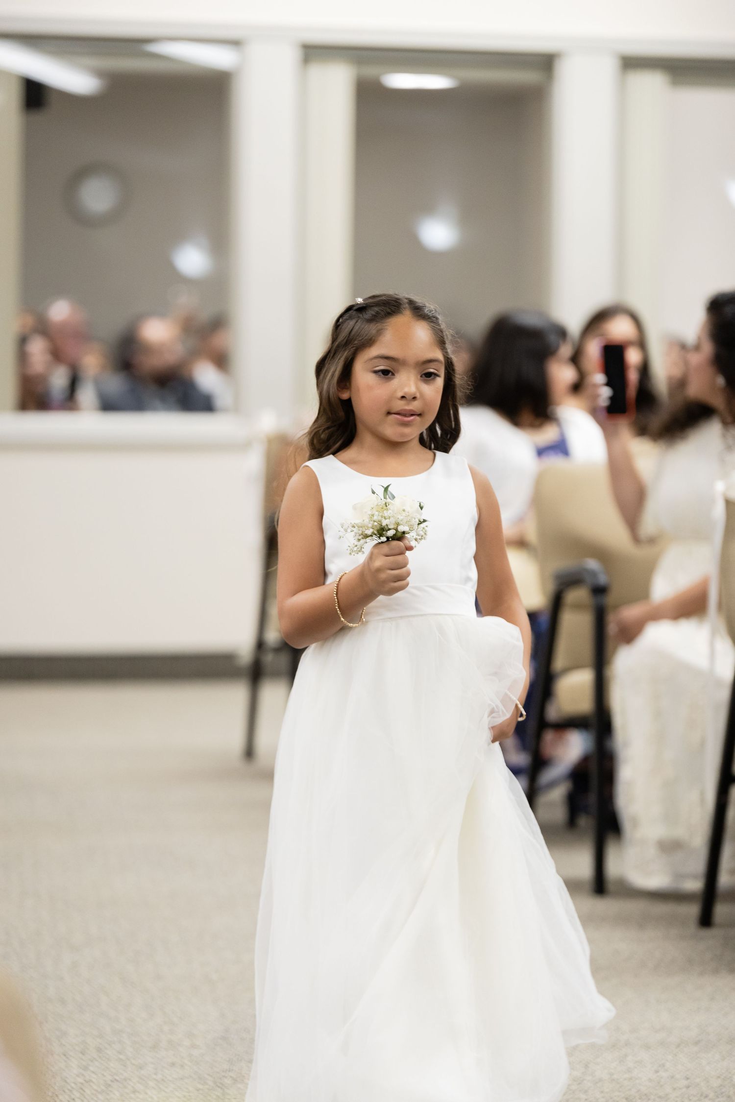 Young attendants in white dresses walking through a carpeted hallway during a formal event.