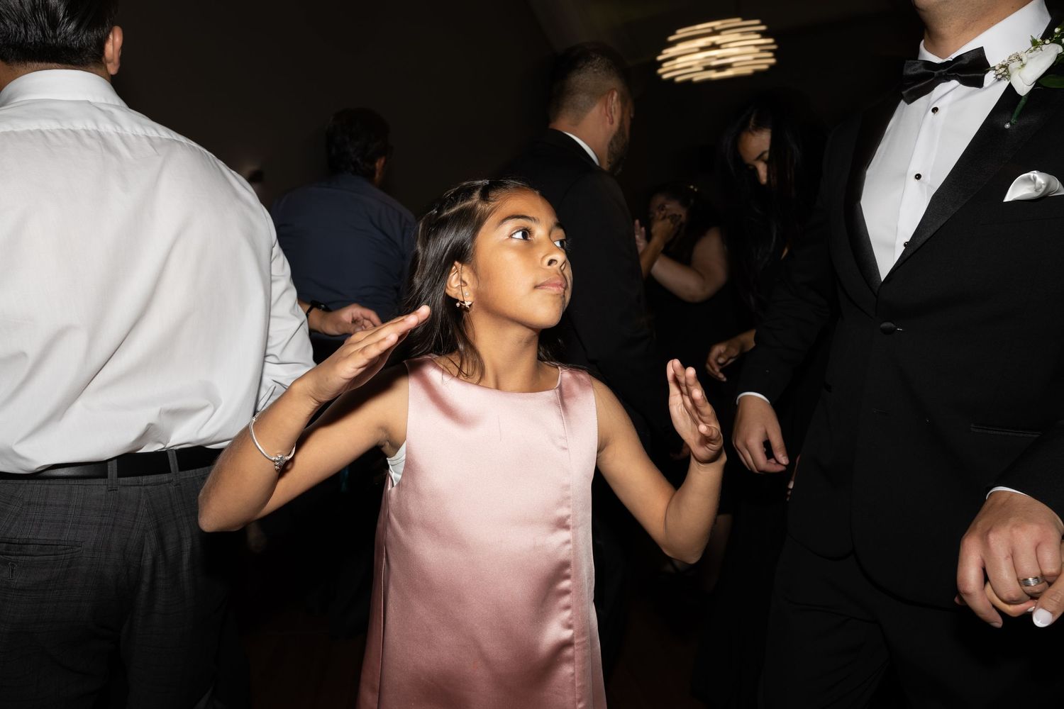 Young guest in pink dress dances enthusiastically at wedding reception.