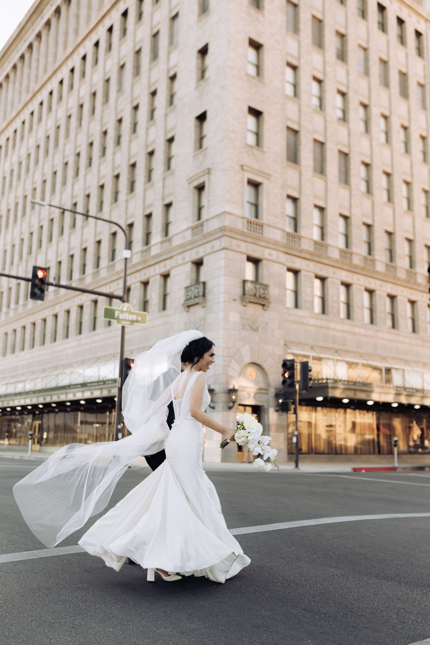 Bride's dress flows dramatically as she twirls on a city street near historic architecture.