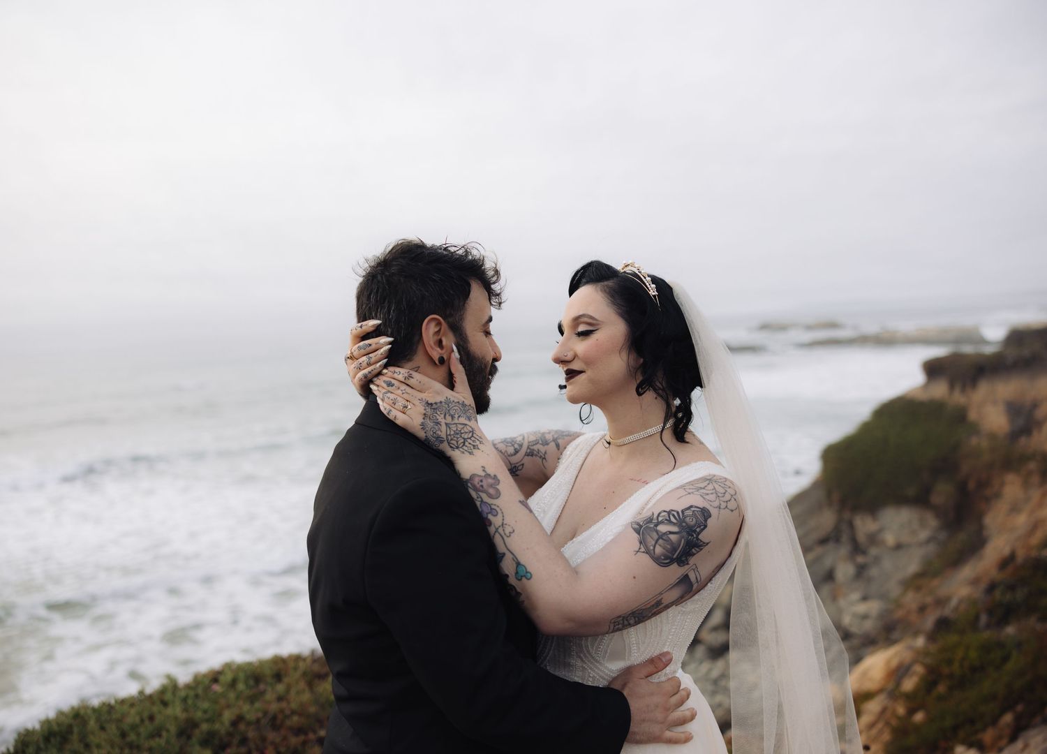 A romantic wedding couple embraces on a dramatic coastal cliff overlooking the ocean.