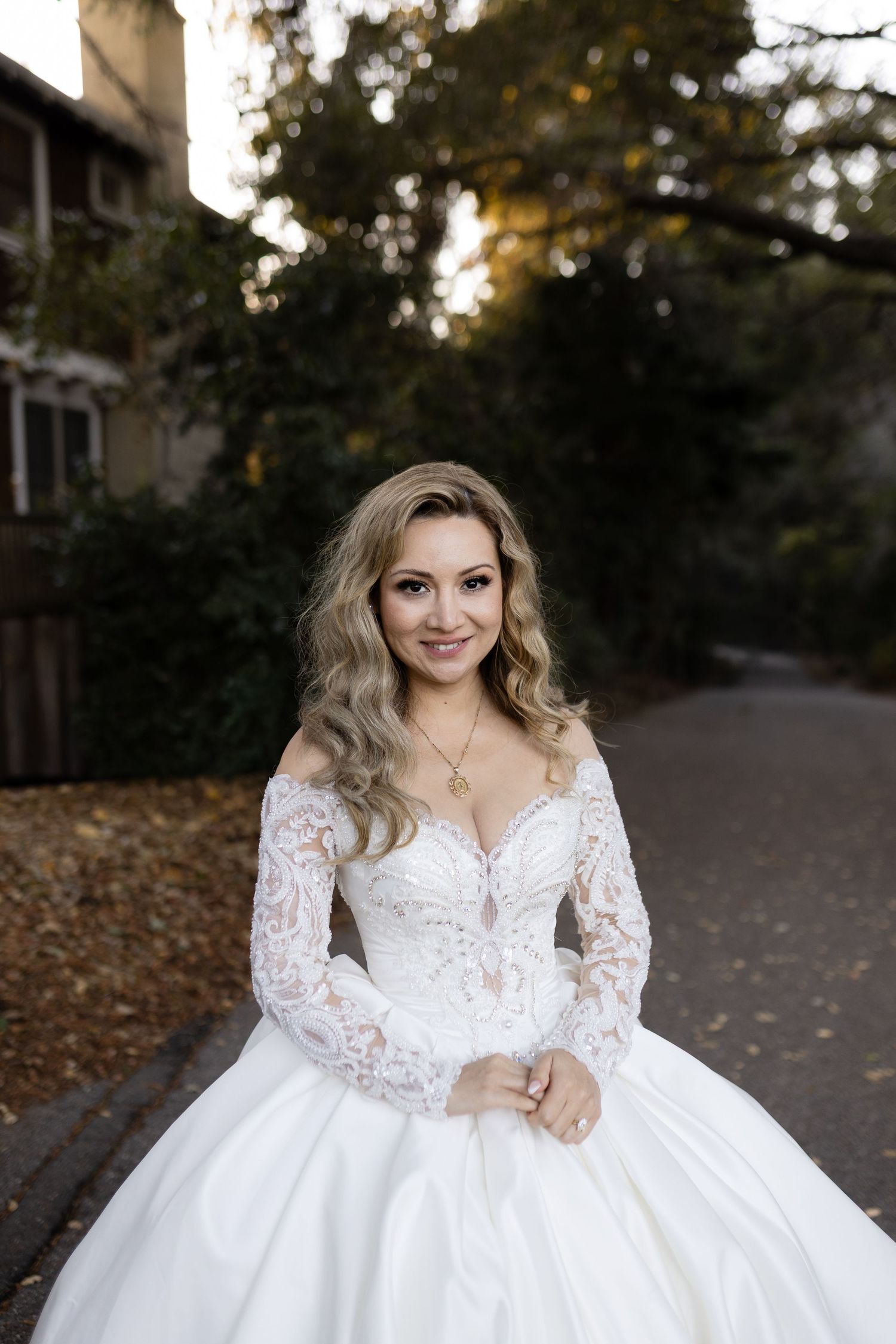 A stunning bridal portrait showcasing an elegant lace-sleeved ball gown in a natural outdoor setting.