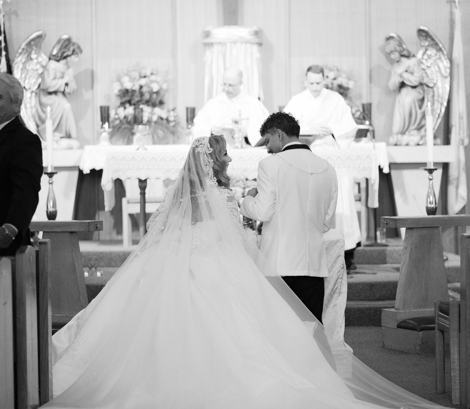 A black and white photograph of a wedding ceremony at a church altar with angel statues.