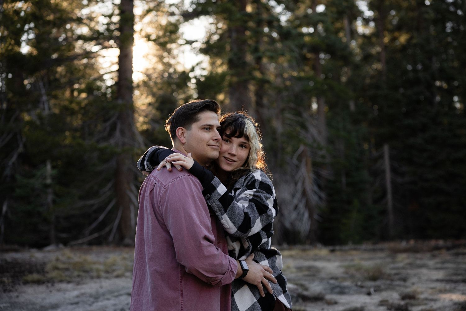 A loving embrace captured in a mountain forest setting during golden hour.