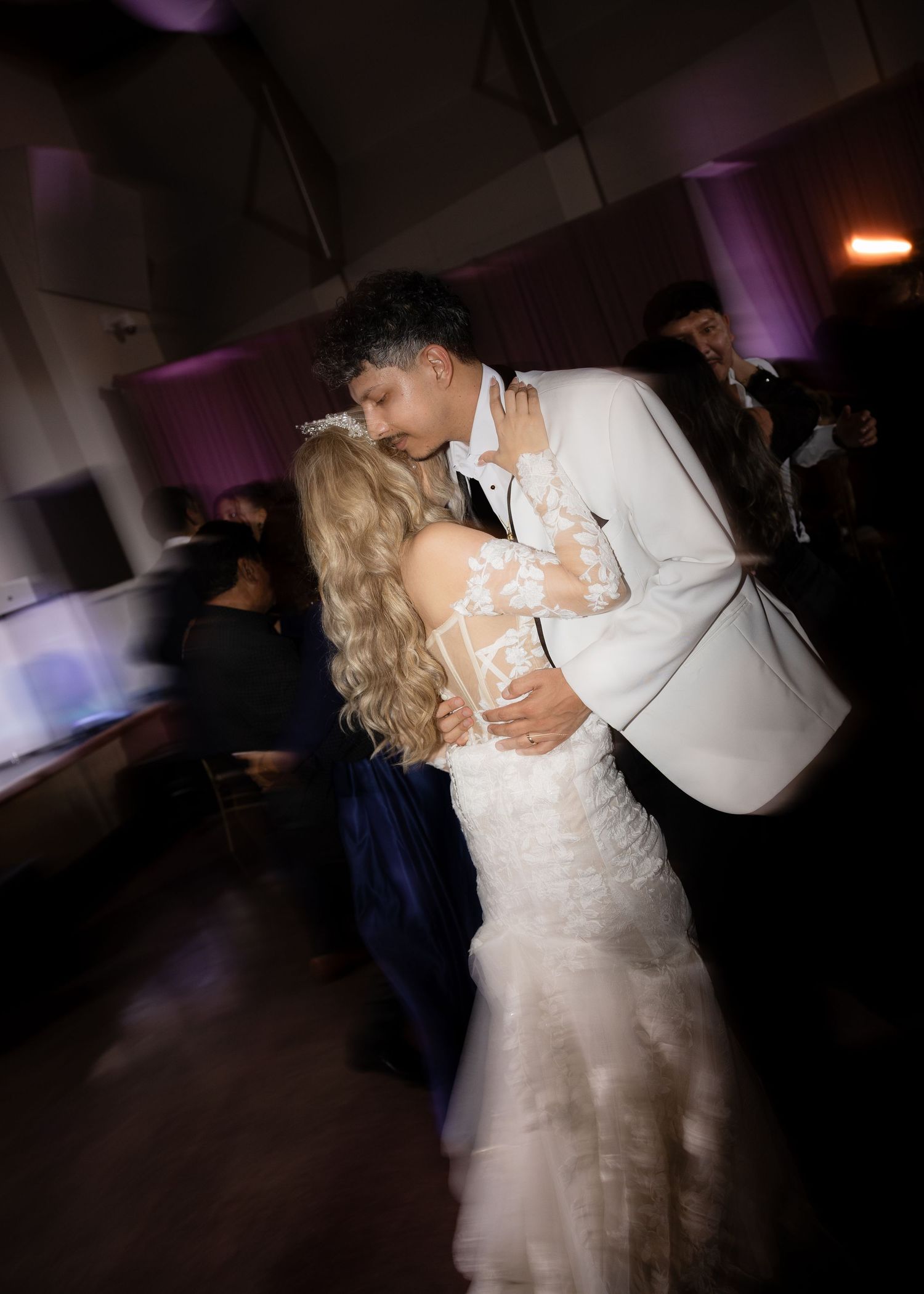 Couple shares romantic dance moment under purple lighting at wedding reception.