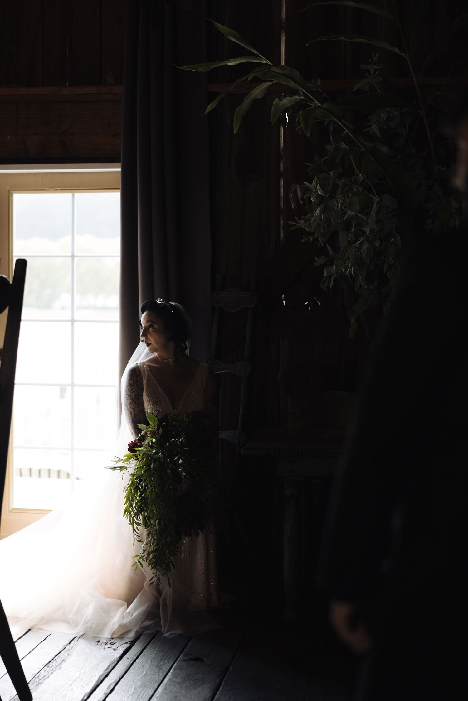 Silhouette of a wedding dress against bright window light in a shadowy interior.