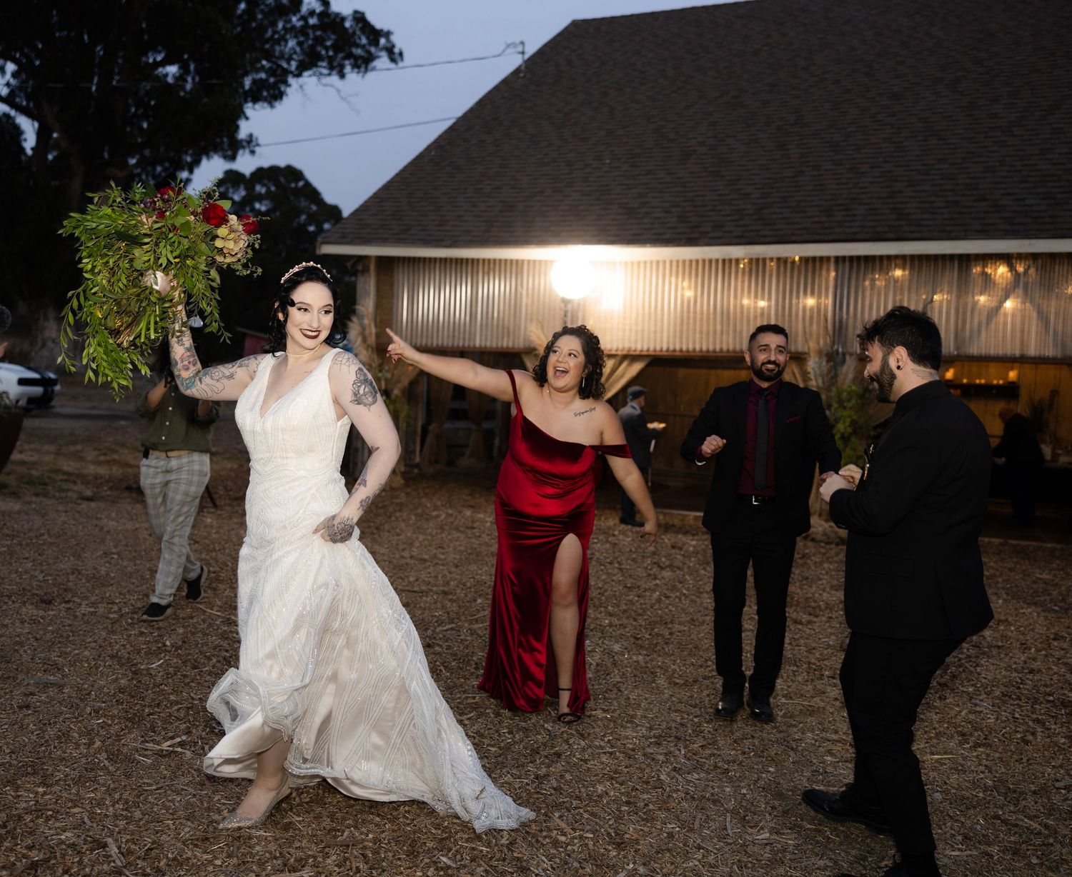 Lively wedding reception with guests dancing outside illuminated barn.