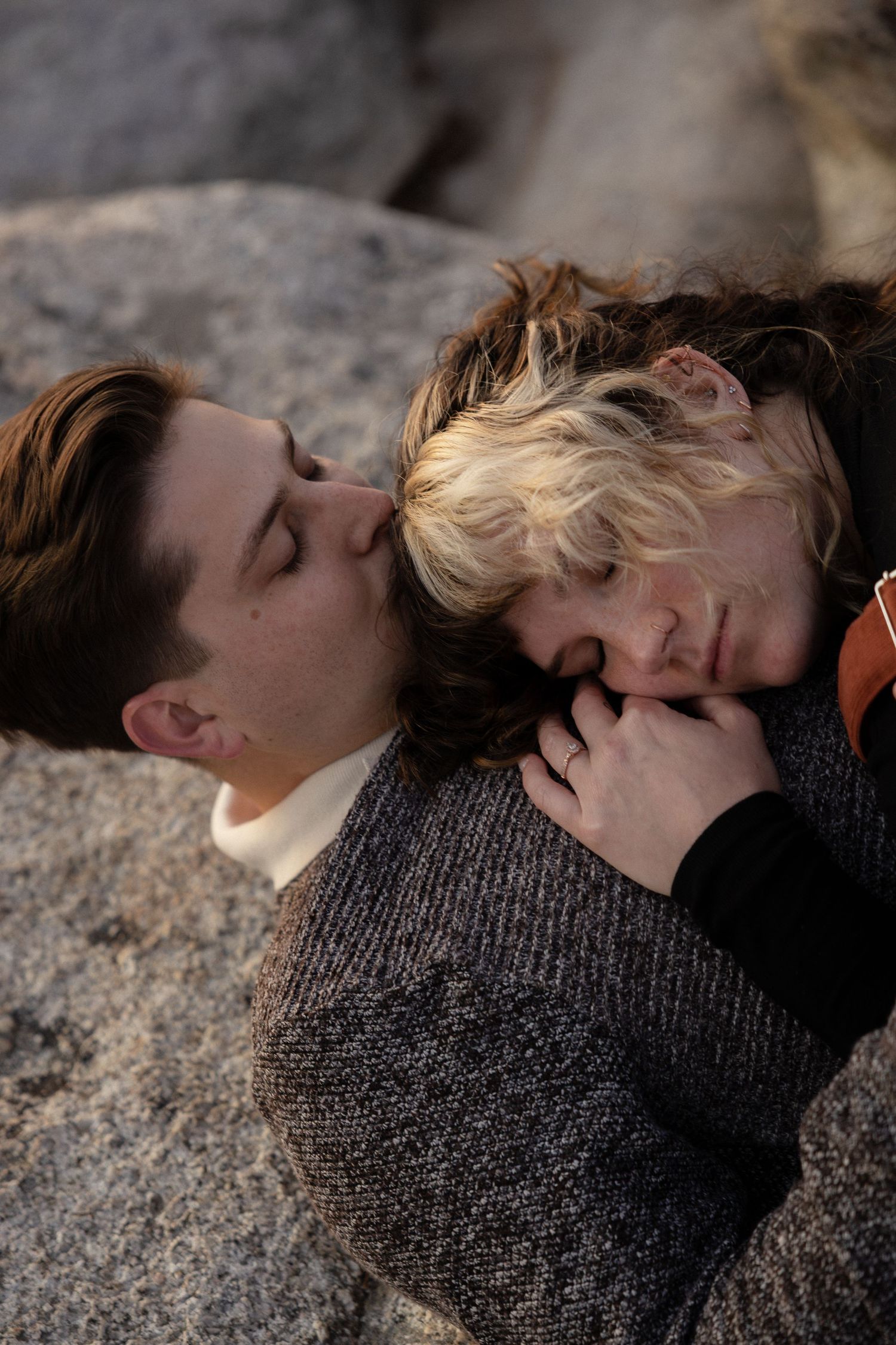 A couple shares a close moment while lying on rocky mountain terrain at sunset.
