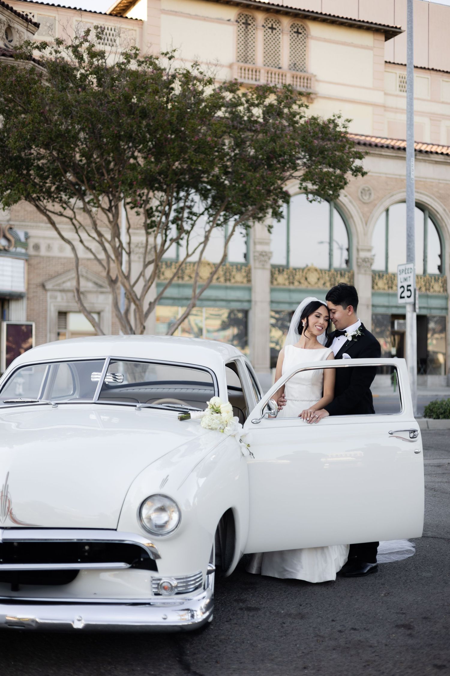 Classic white vintage car serves as wedding transportation against architectural backdrop.