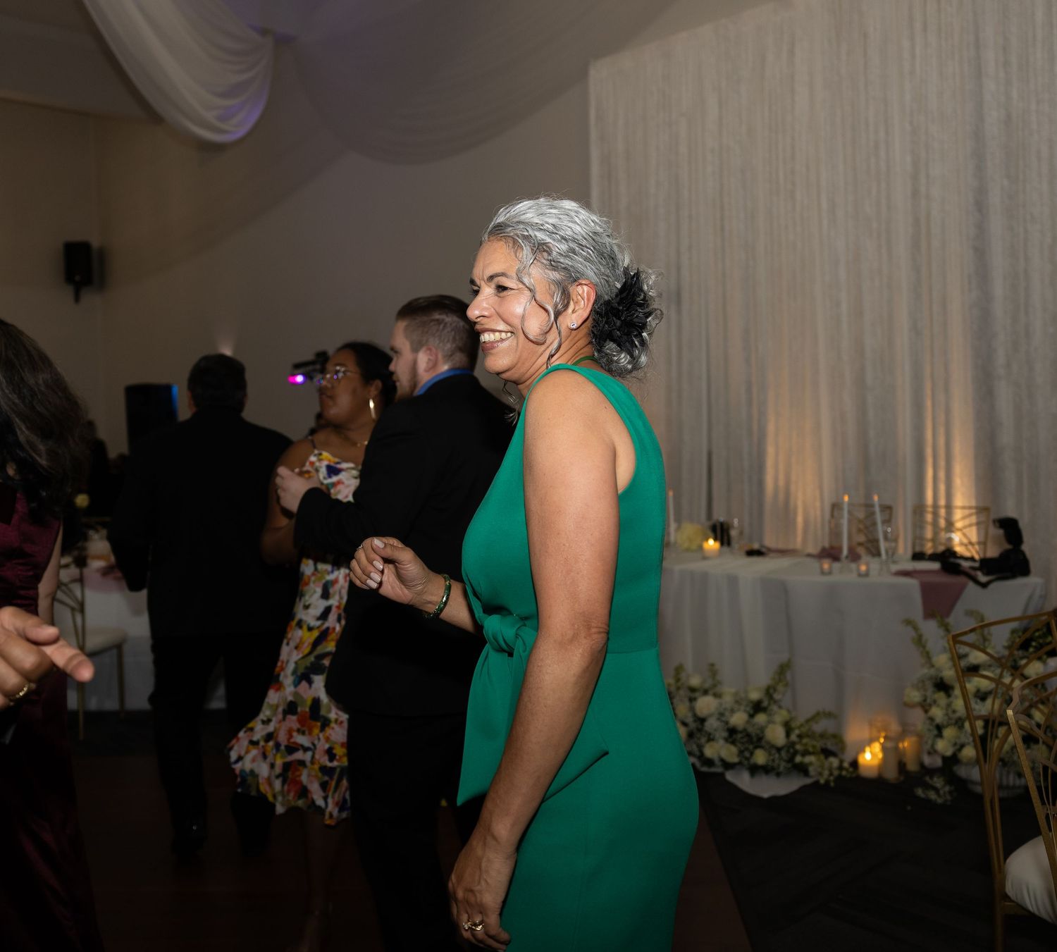 Wedding guests dancing together at an indoor reception venue with white draping.