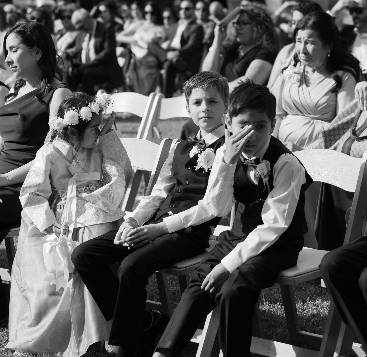 Black and white photo of children seated at an outdoor wedding ceremony, including a flower girl with floral crown.