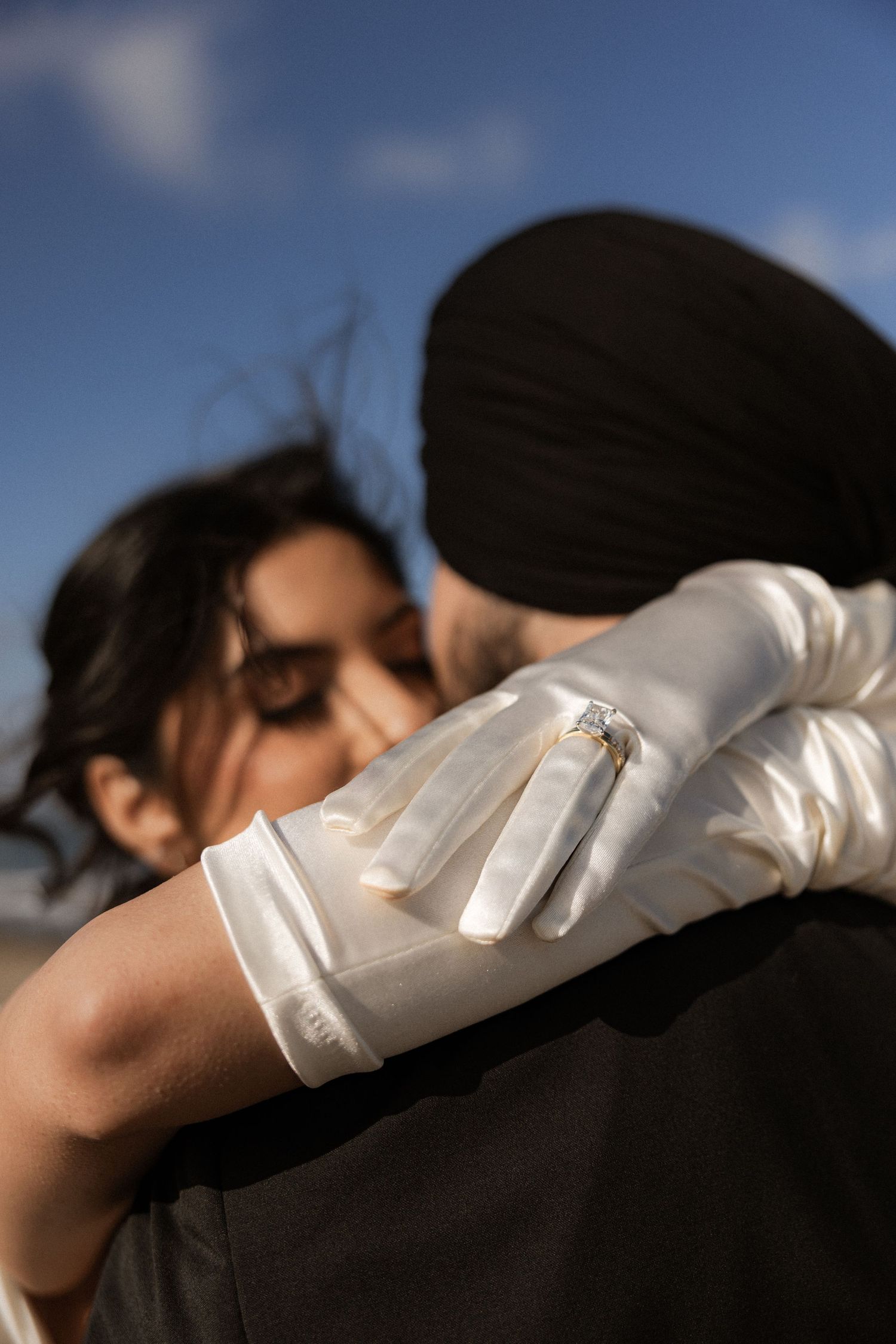 A couple embraces in silhouette against a bright blue sky background.