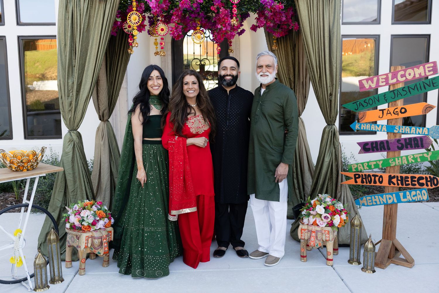 A festive group photo with traditional outfits in front of decorative holiday decor with green curtains and signs.