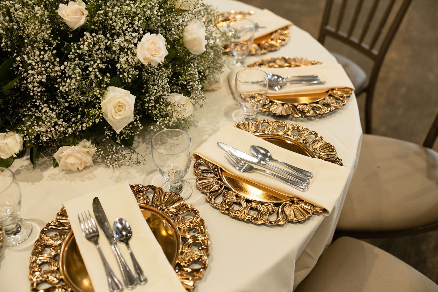 Elegant table settings with white linens, gold chargers, and floral centerpieces at a formal event.