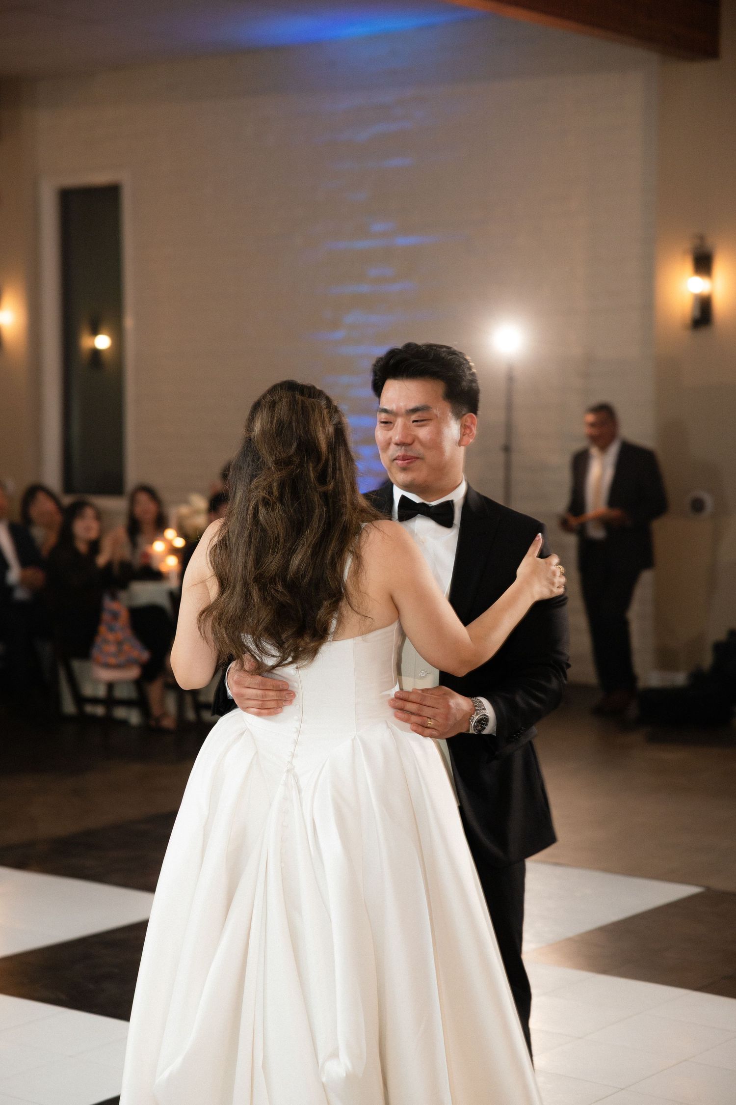 Bride and groom sharing intimate first dance on checkered floor at elegant wedding reception.